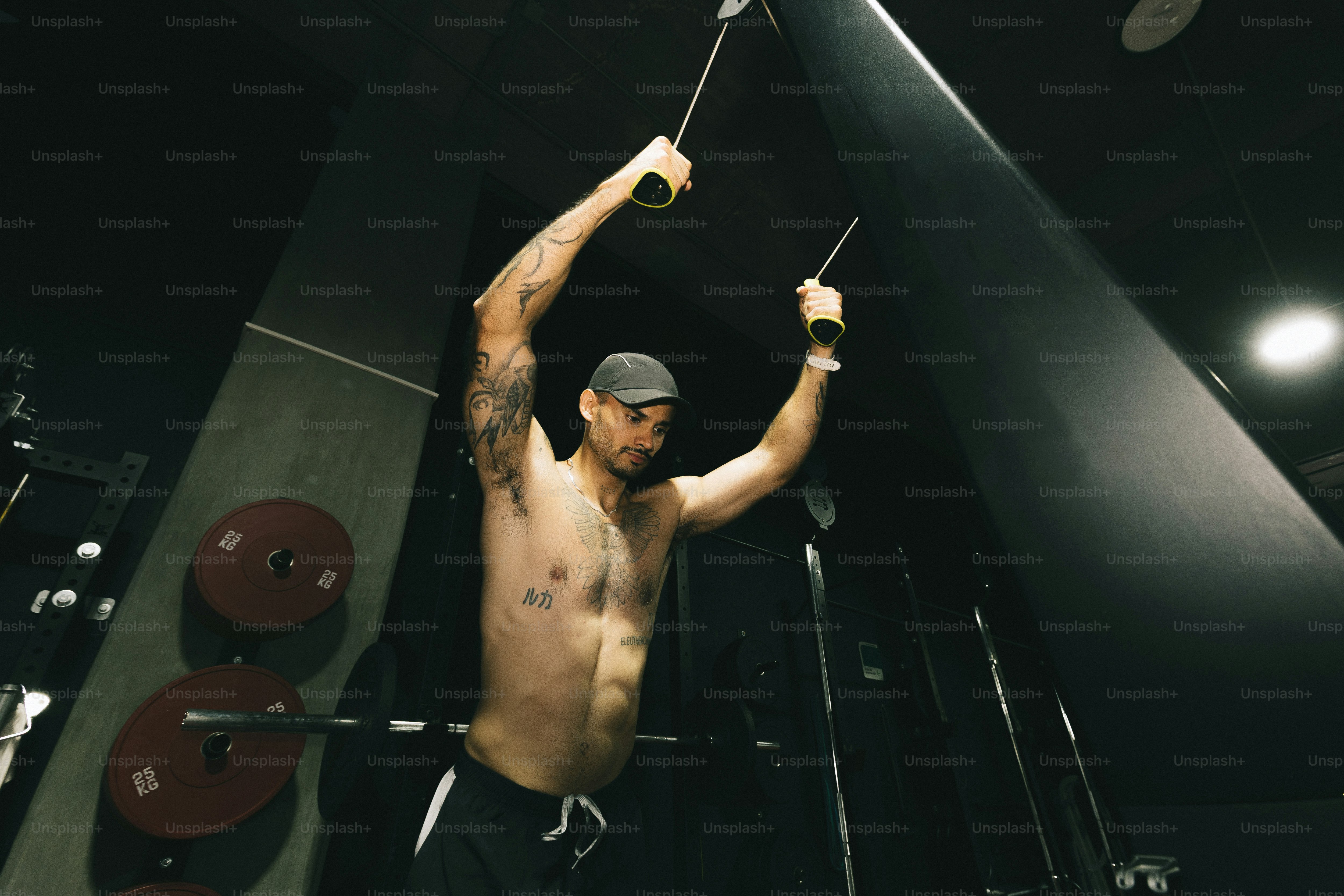 A shirtless man with tattoos performing a cable crossover exercise in a gym