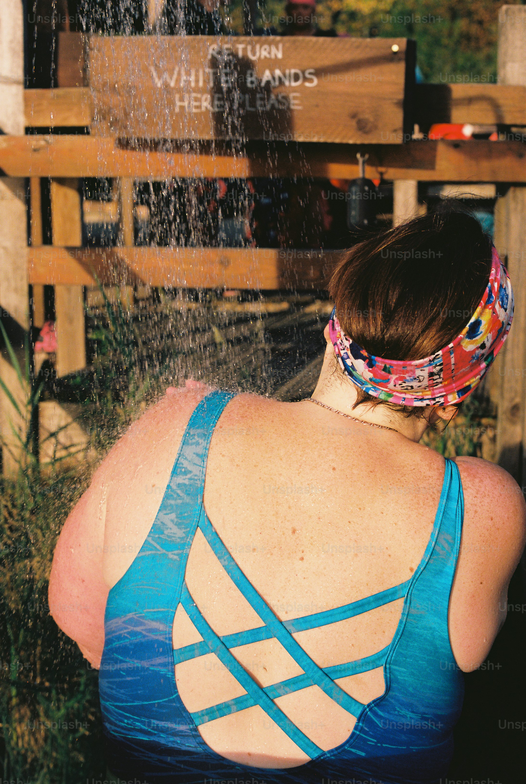 A woman in a blue swimsuit rinsing under an outdoor shower.