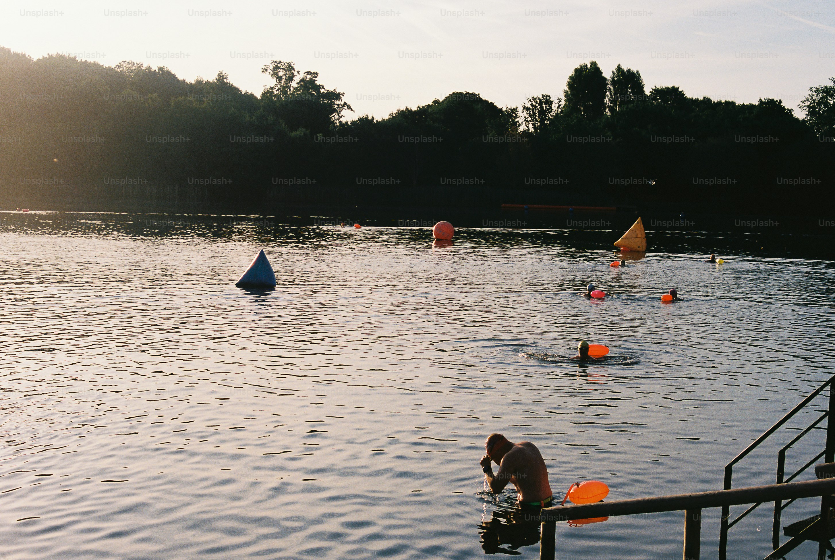 A person swimming in a lake with colorful buoys under low golden light.
