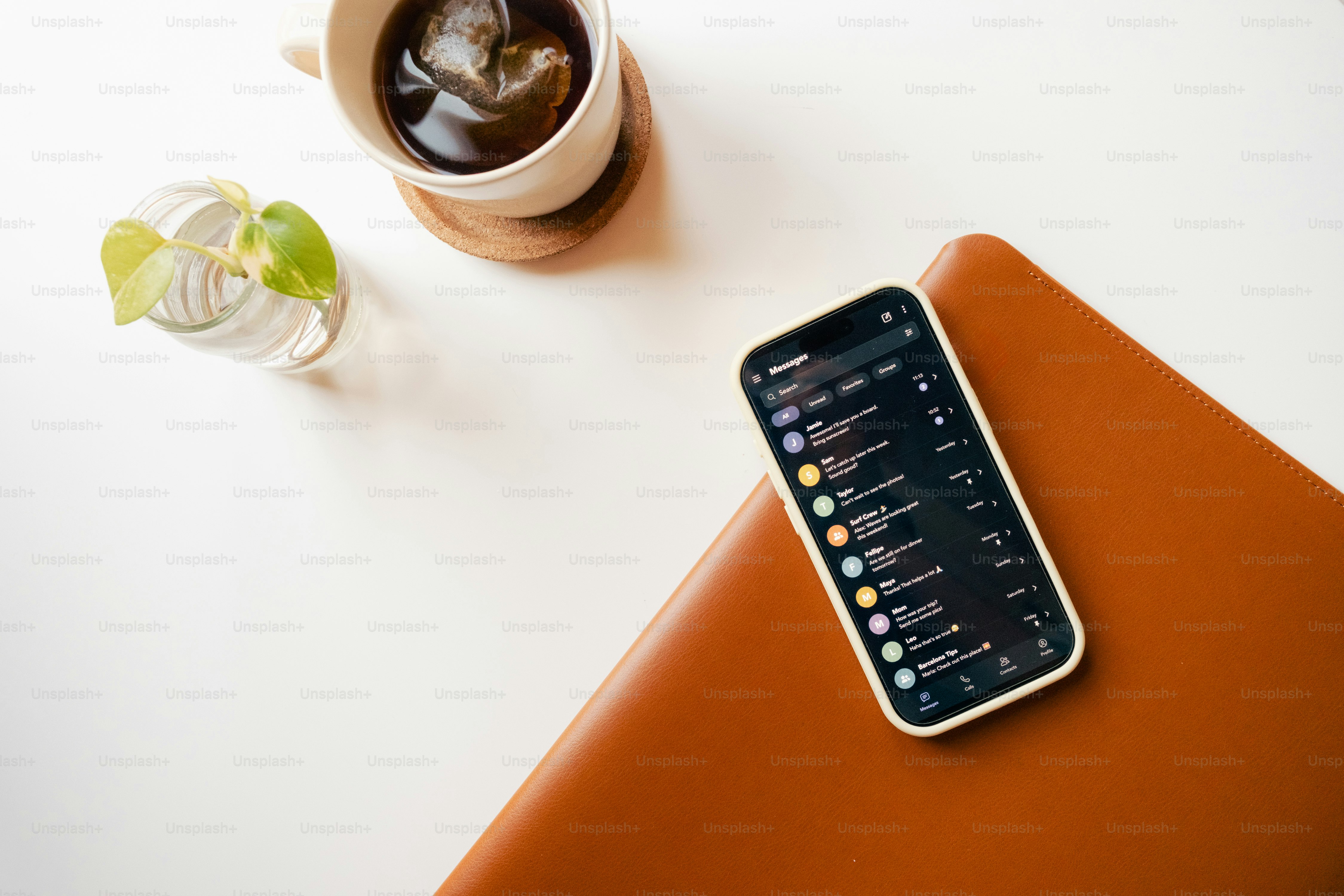 A smartphone displaying a messaging app on a brown leather notebook beside coffee