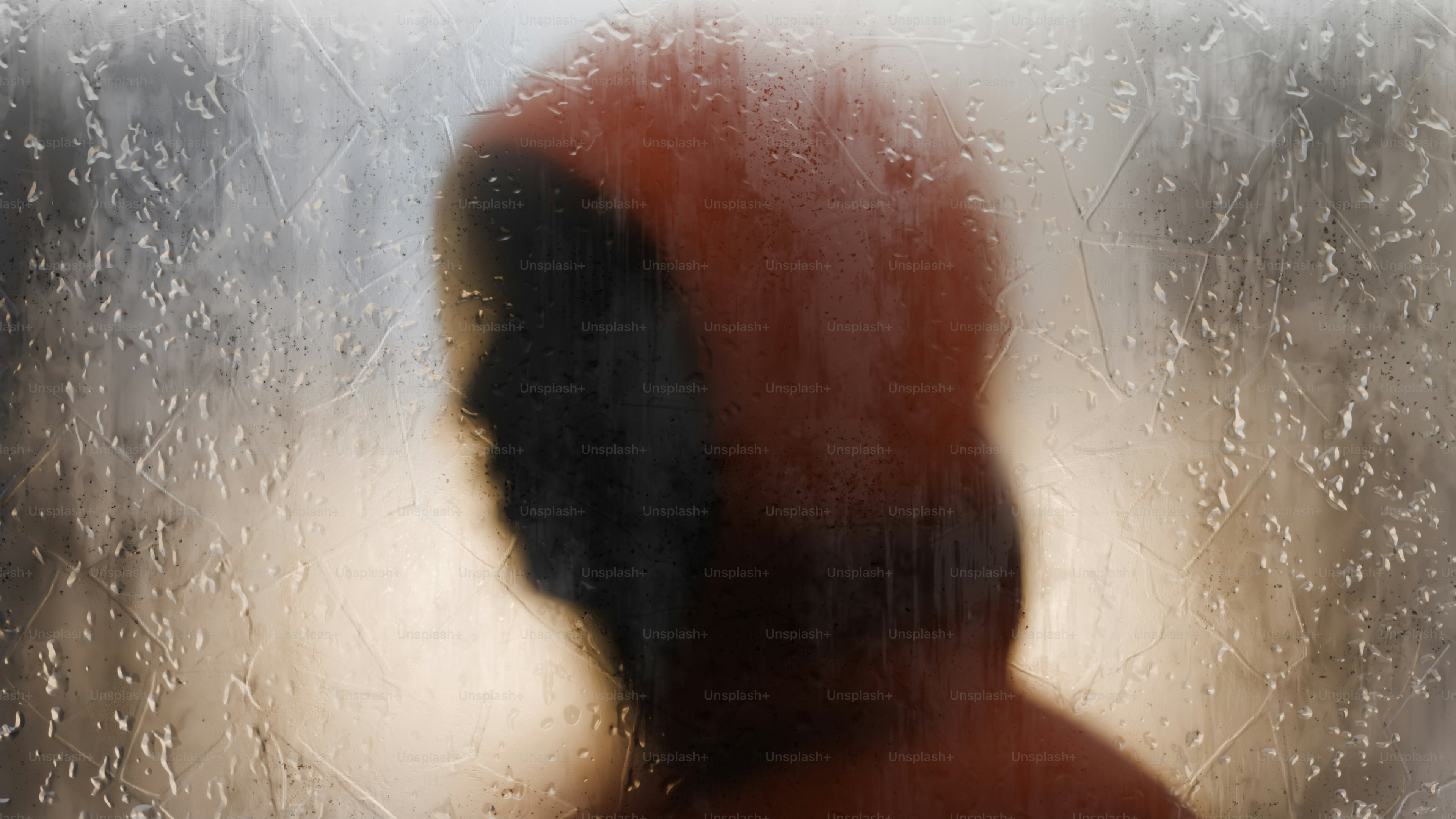 Eine Silhouette einer Person mit Kapuze hinter einer regenverschmierten Glasscheibe
