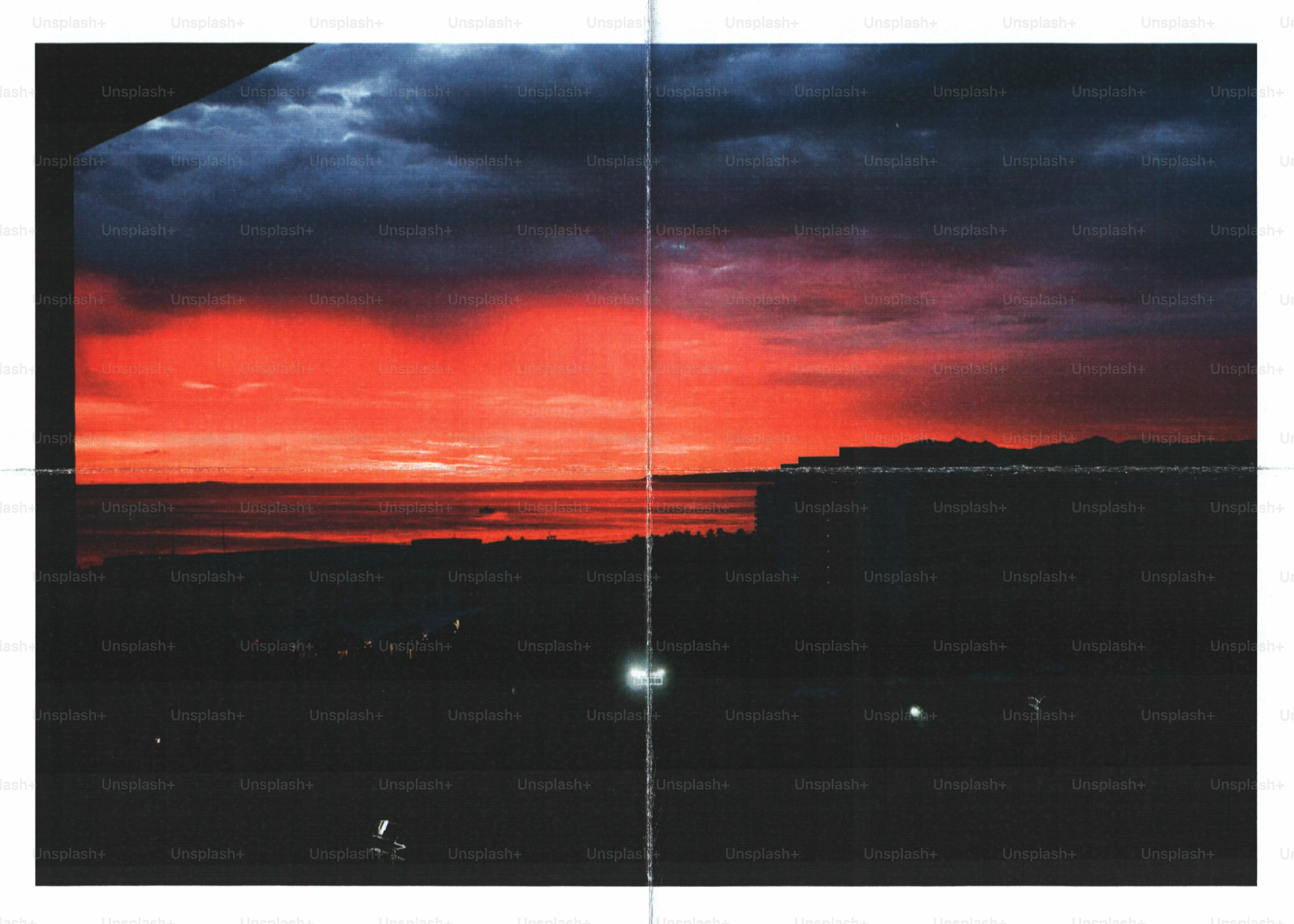 A vibrant red sky over a dark sea and distant coastline at low light