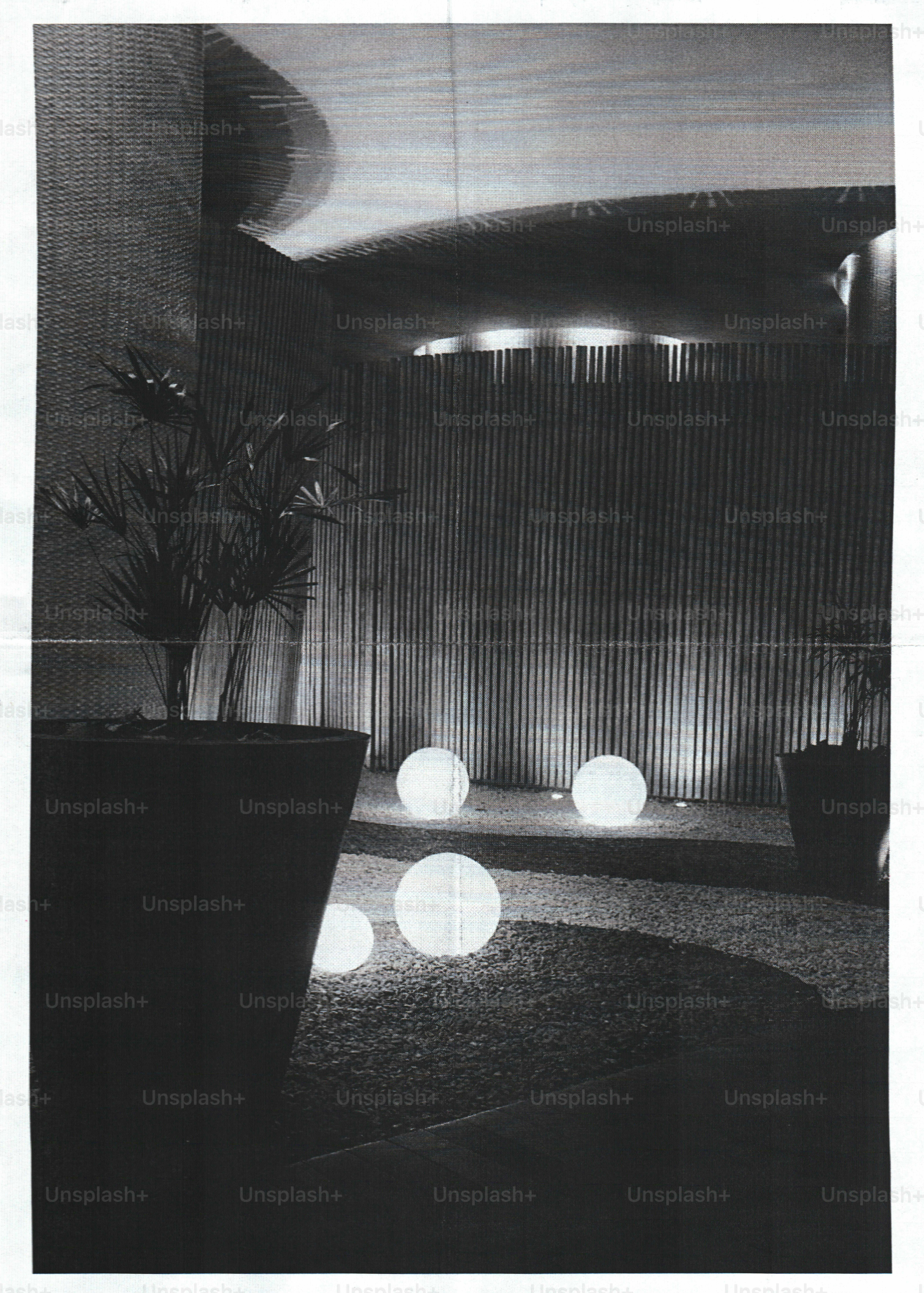 Glowing spherical lights on a gravel path beside potted plants in a dark space