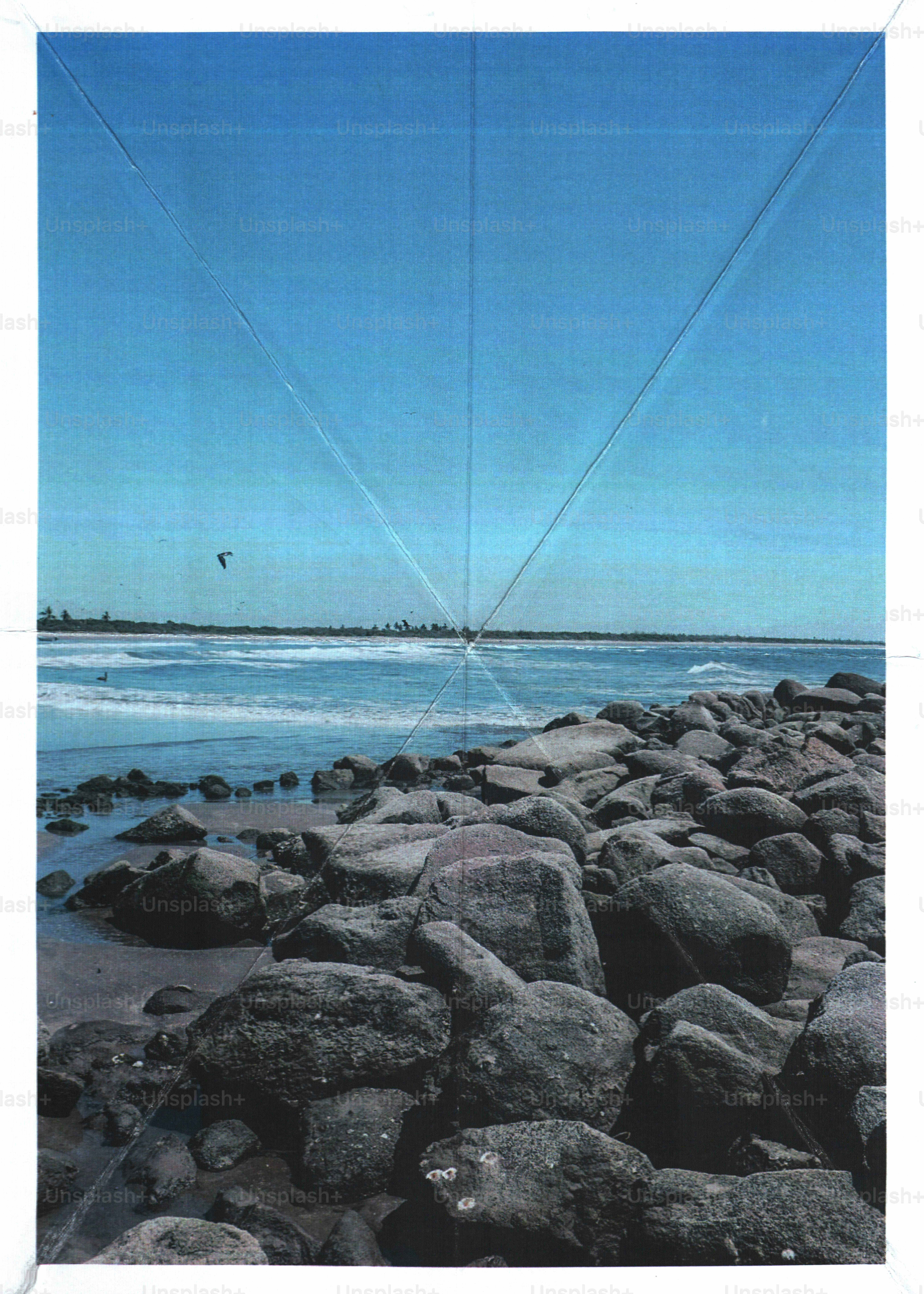 Large dark rocks along a sandy beach meeting the blue ocean under clear skies