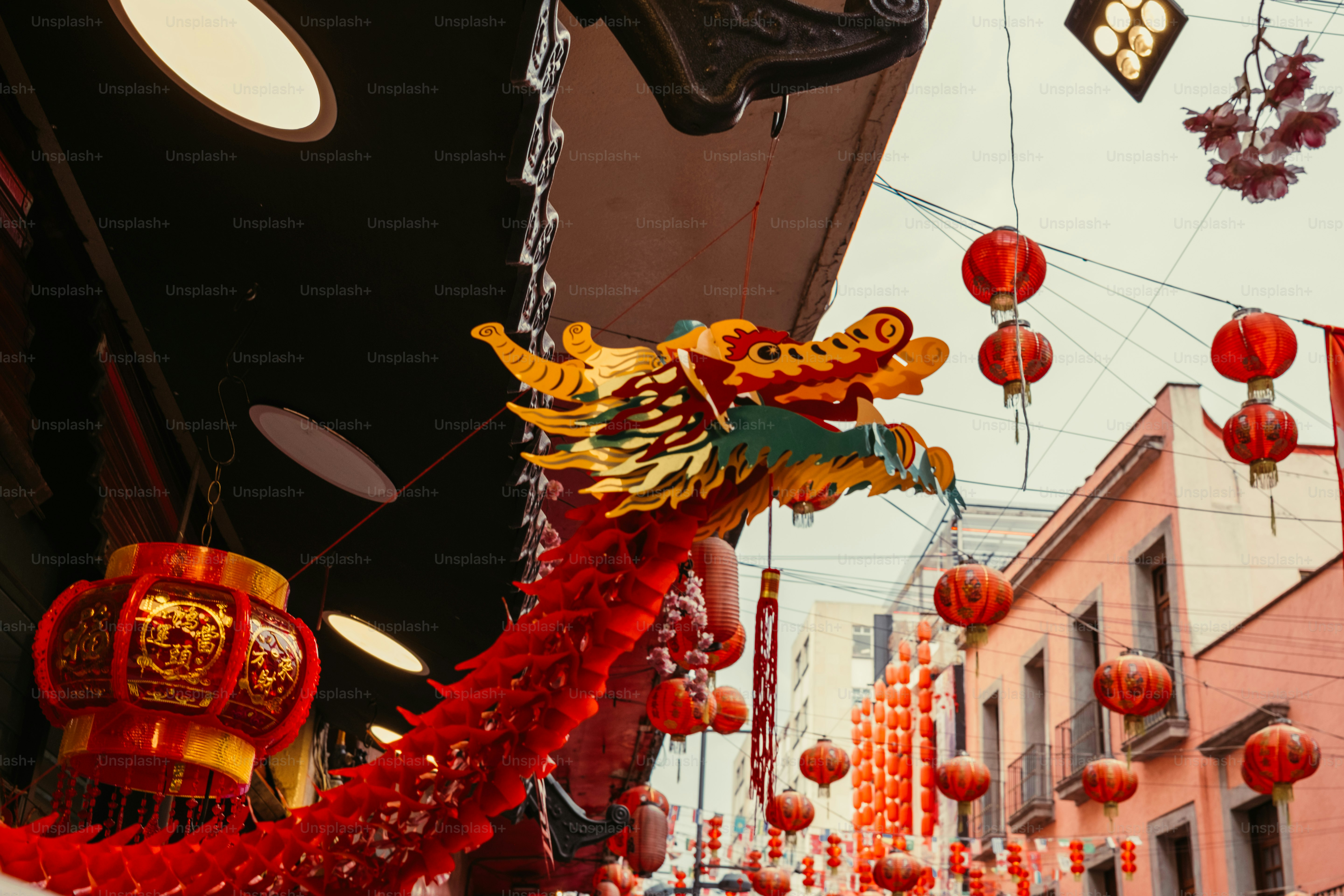 Une sculpture décorative de tête de dragon suspendue au-dessus de lanternes rouges dans une rue de la ville