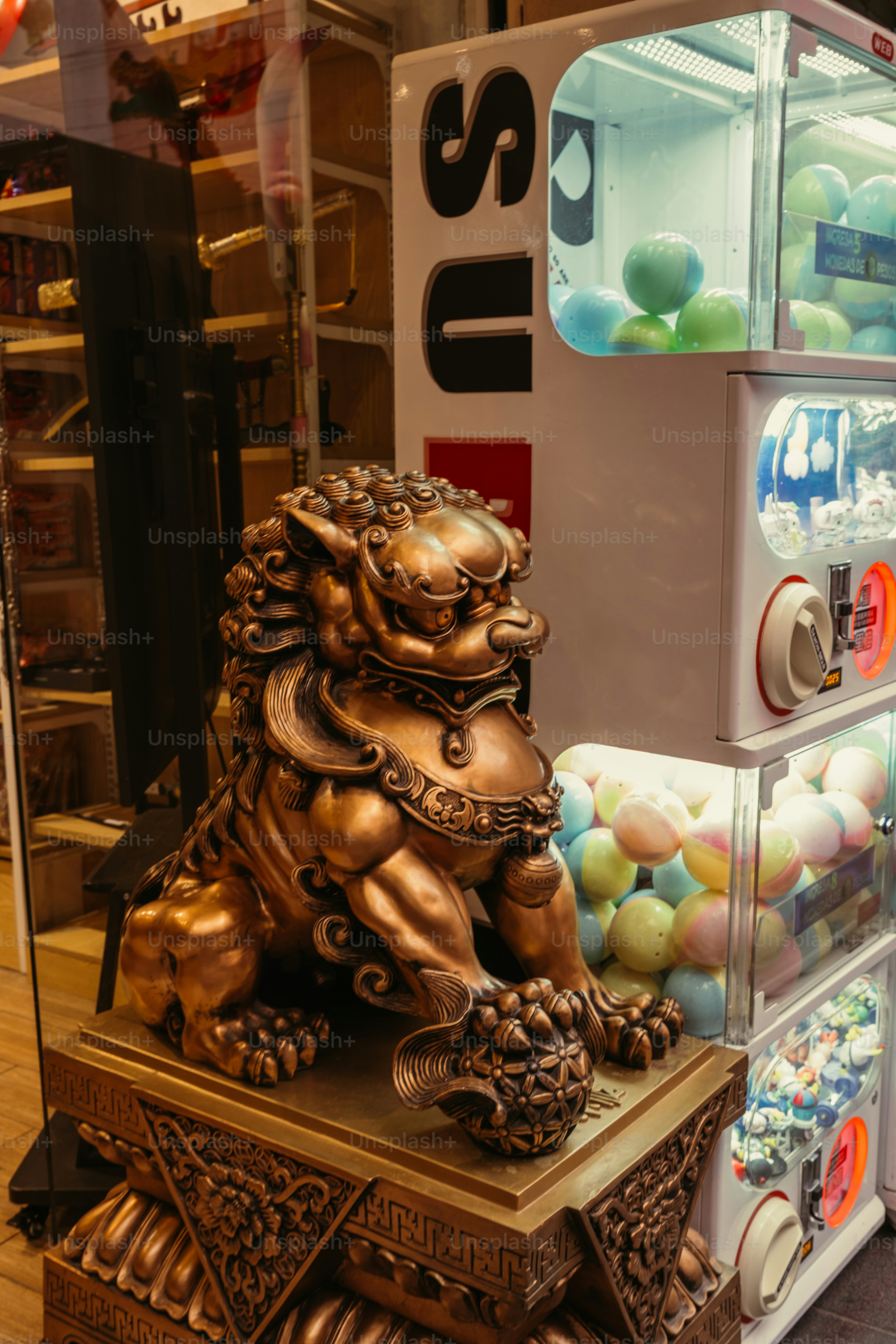 Eine bronzene Wächterlöwenstatue neben einem weißen Verkaufsautomaten, gefüllt mit bunten Kapseln