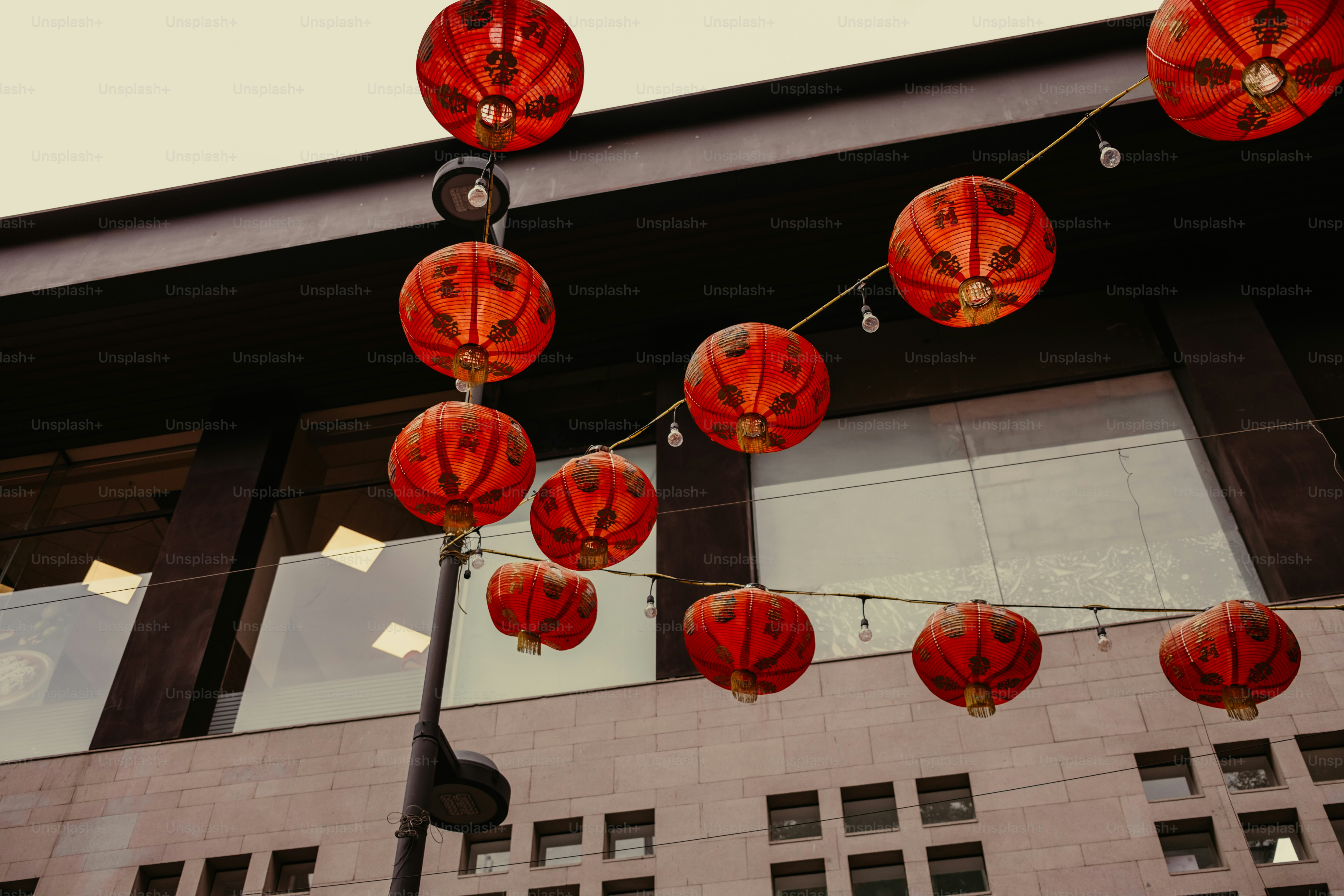 Lanternes en papier rouge suspendues à des ficelles contre une façade moderne de bâtiment