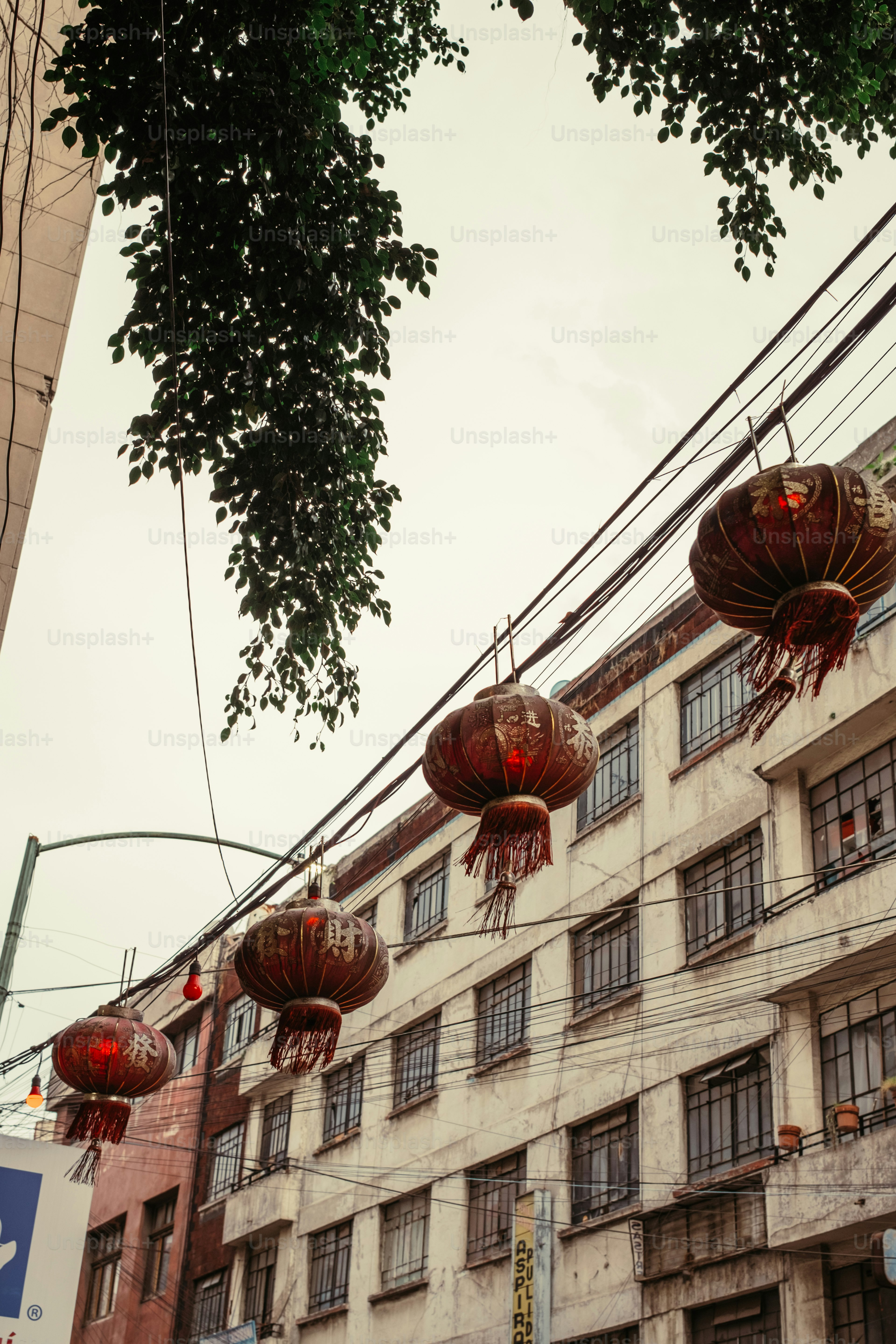 Red paper lanterns hanging from wires above a city street with old buildings