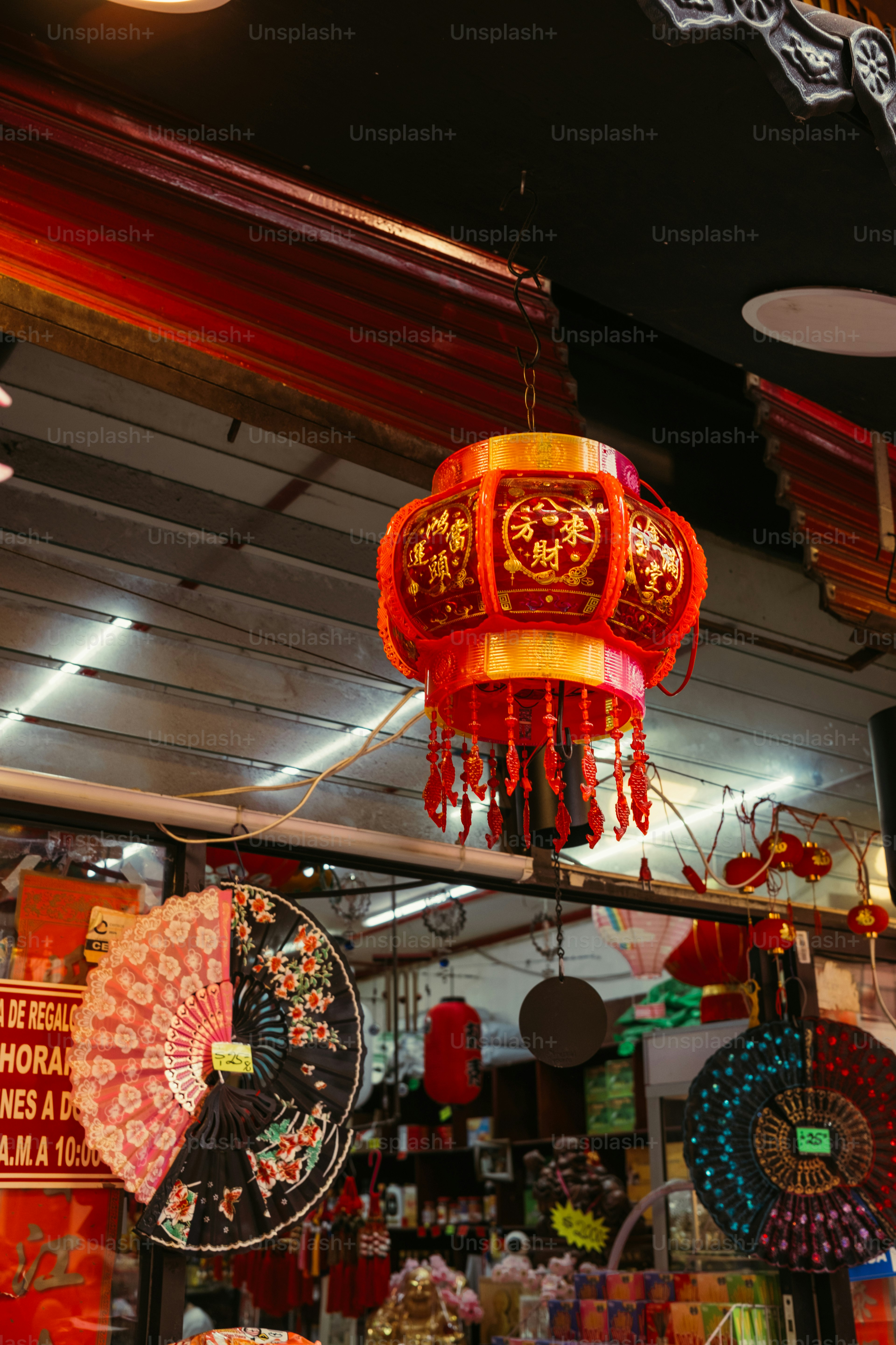 Une lanterne chinoise rouge et or accrochée dans une boutique avec des éventails décoratifs