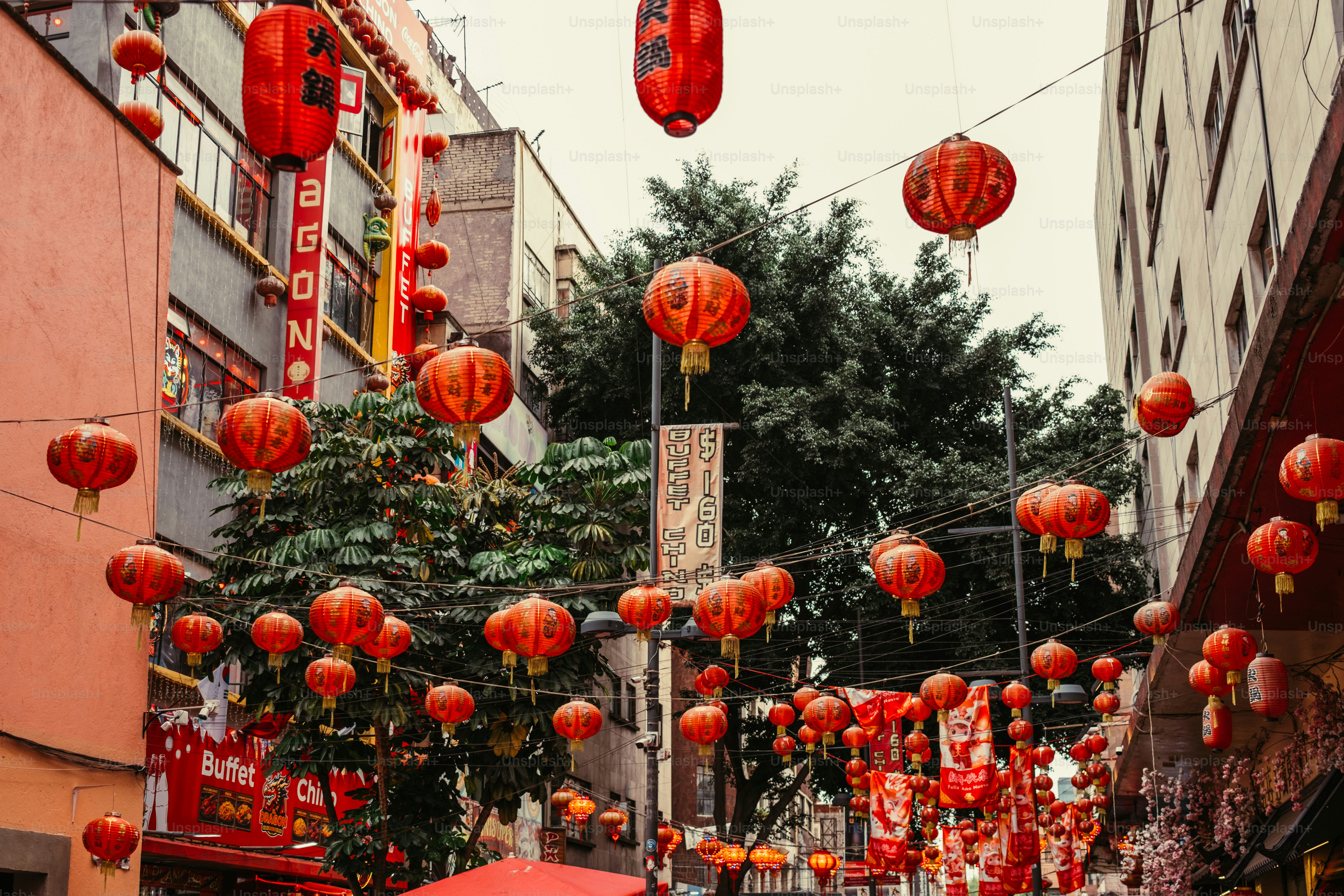 Many red paper lanterns hanging above a narrow city street with buildings
