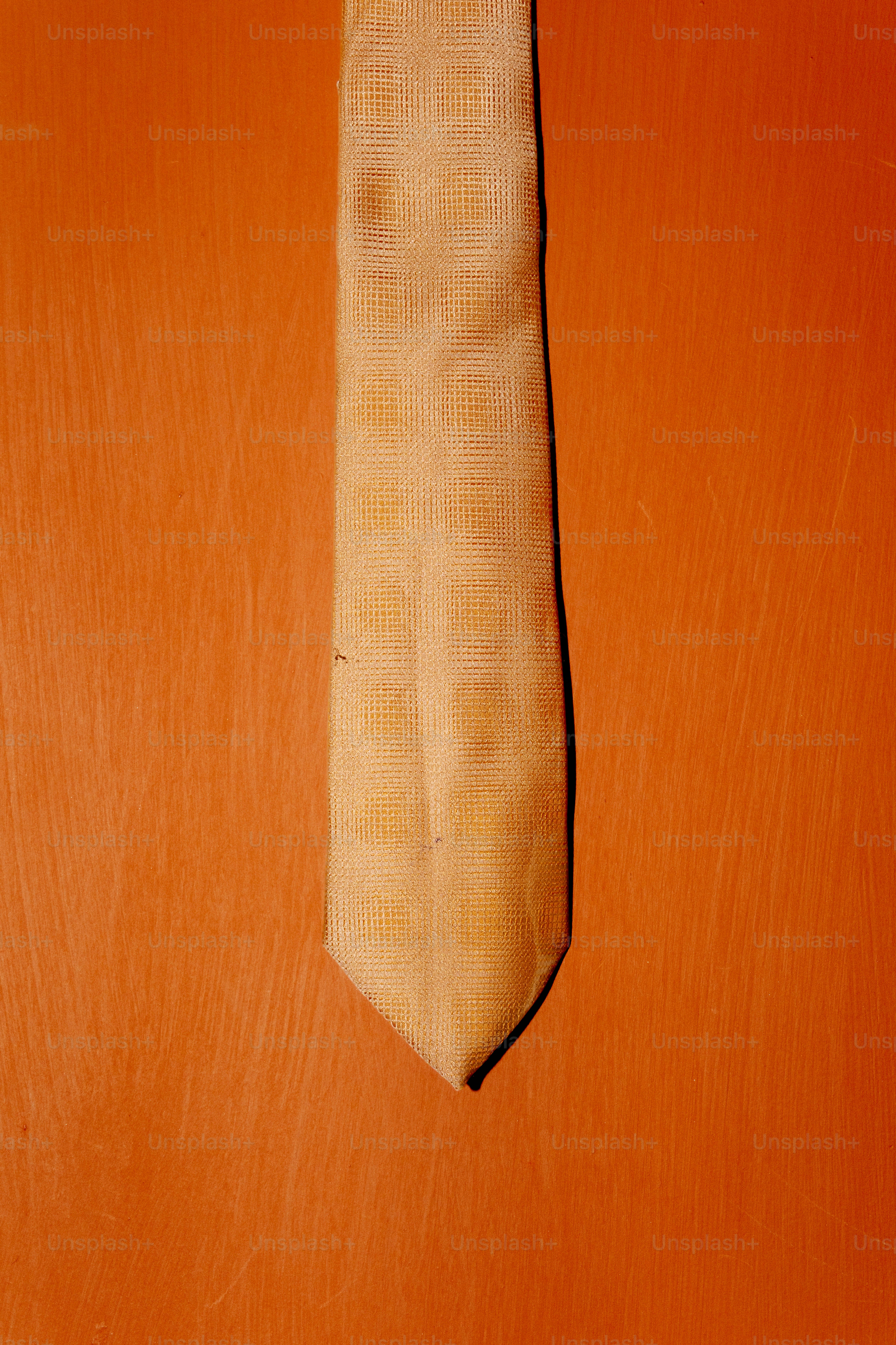 A textured tan necktie centered against a solid orange background