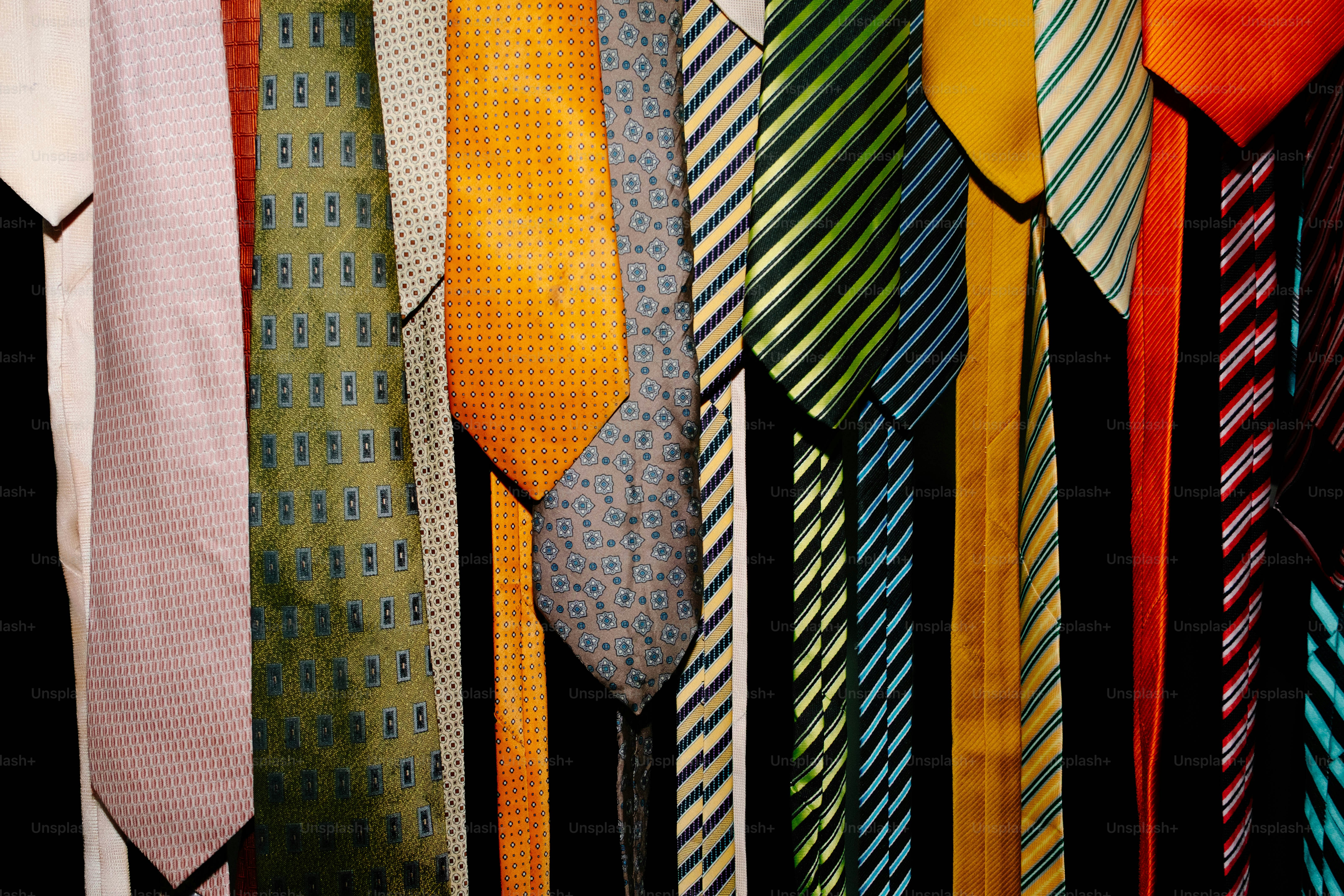 A collection of colorful neckties with various patterns hanging against a black background