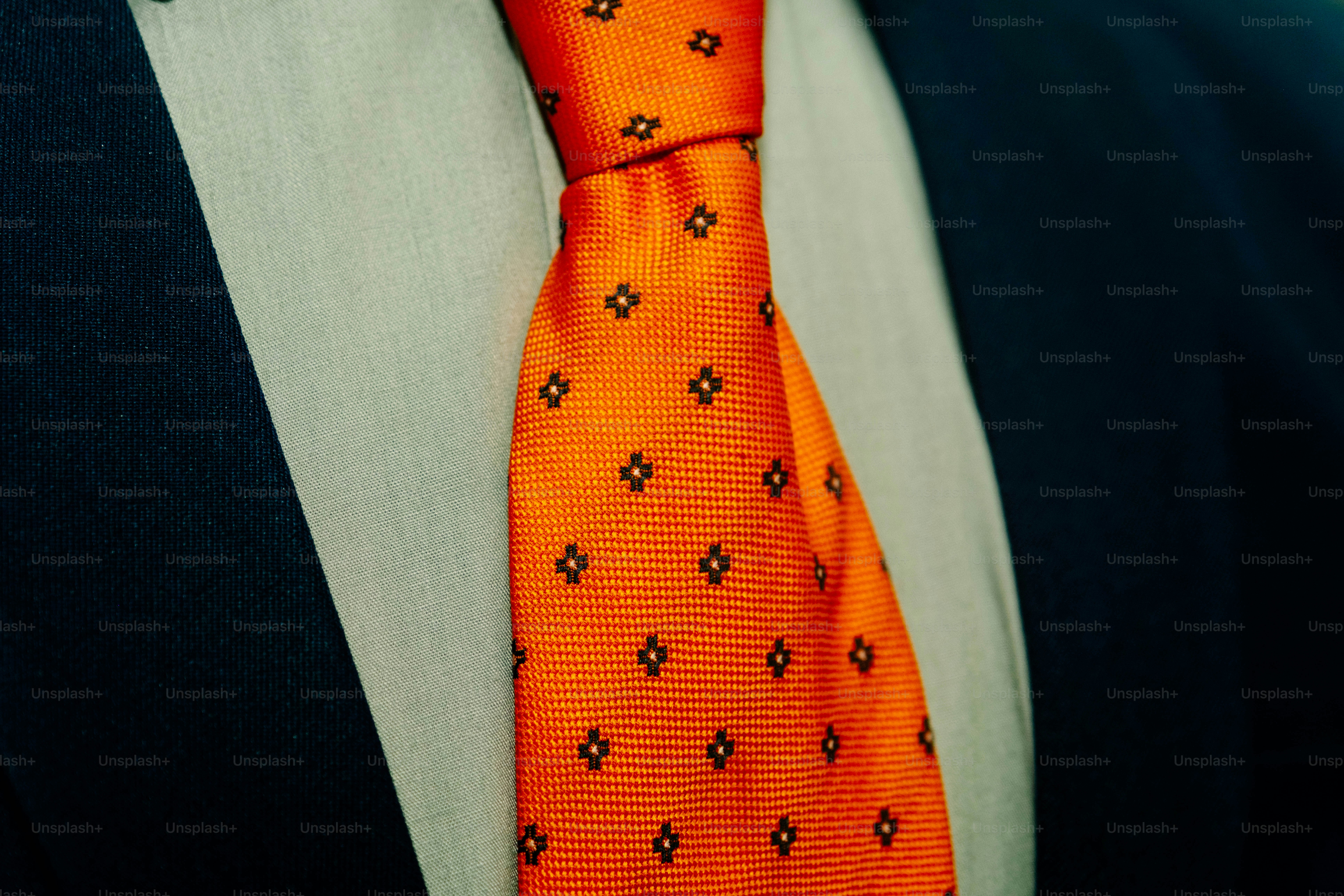 An orange tie with a small dark pattern over a light shirt and jacket