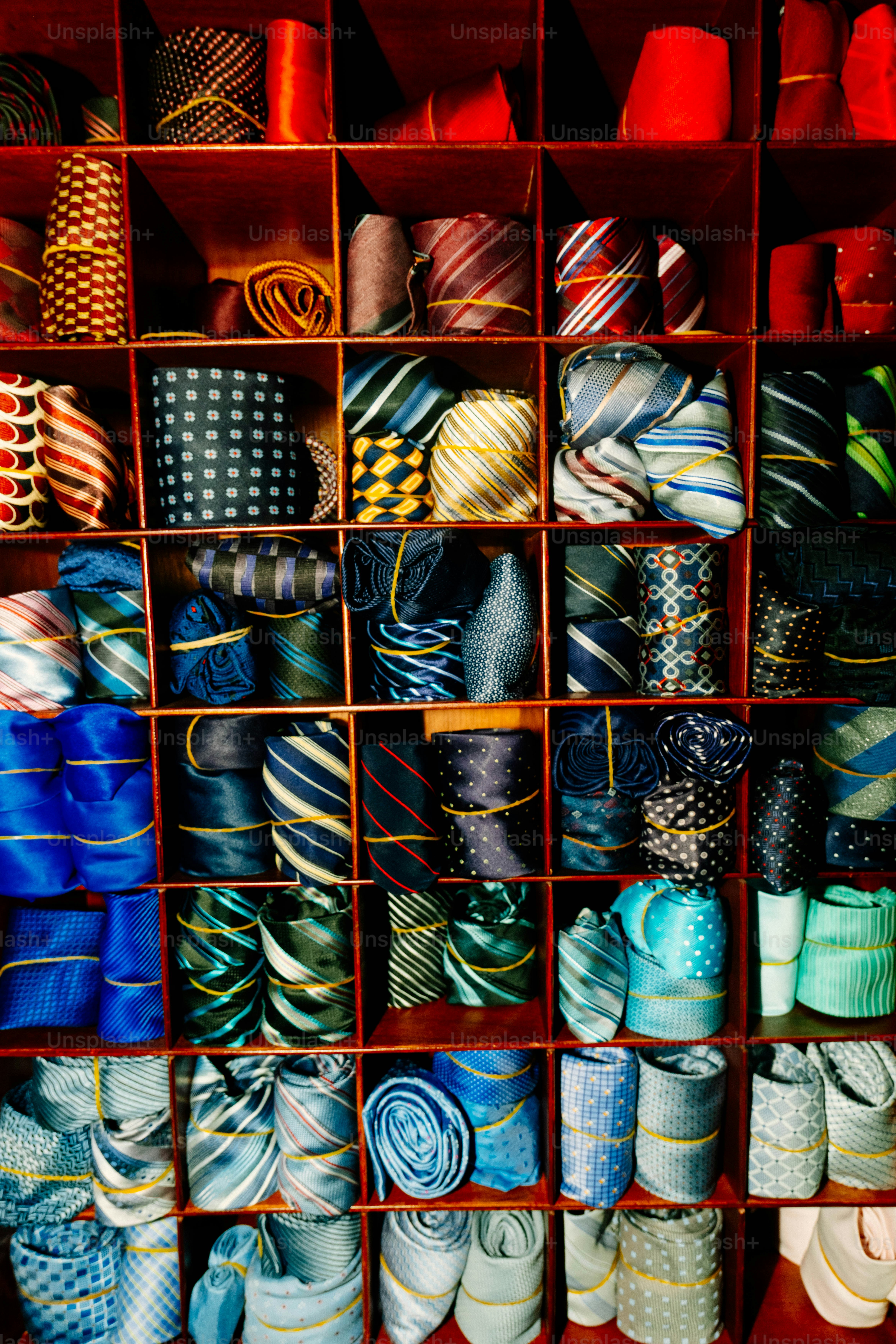 Many rolled neckties in various colors and patterns organized in a wooden grid shelf