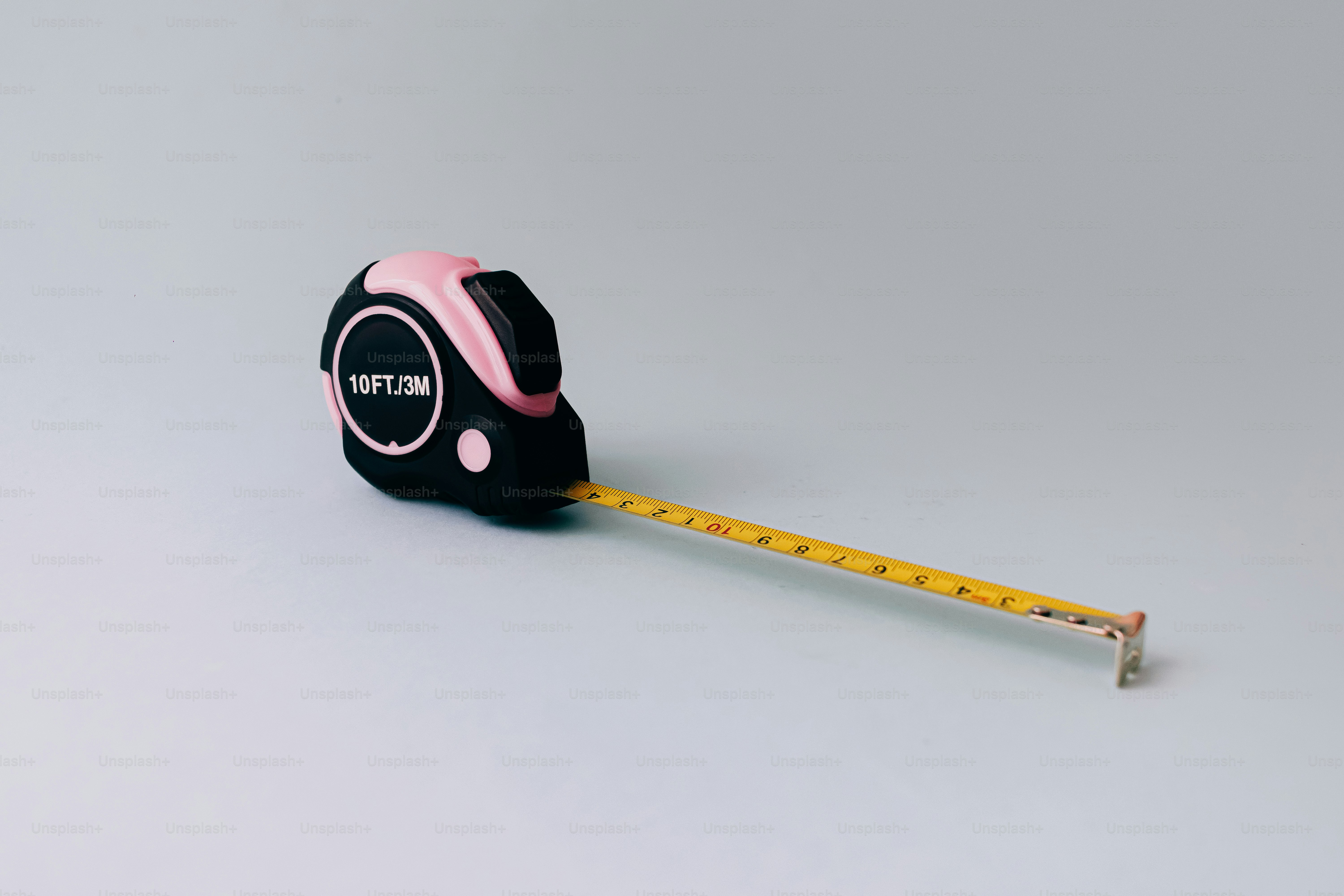 A black and pink tape measure with an extended yellow measuring tape.