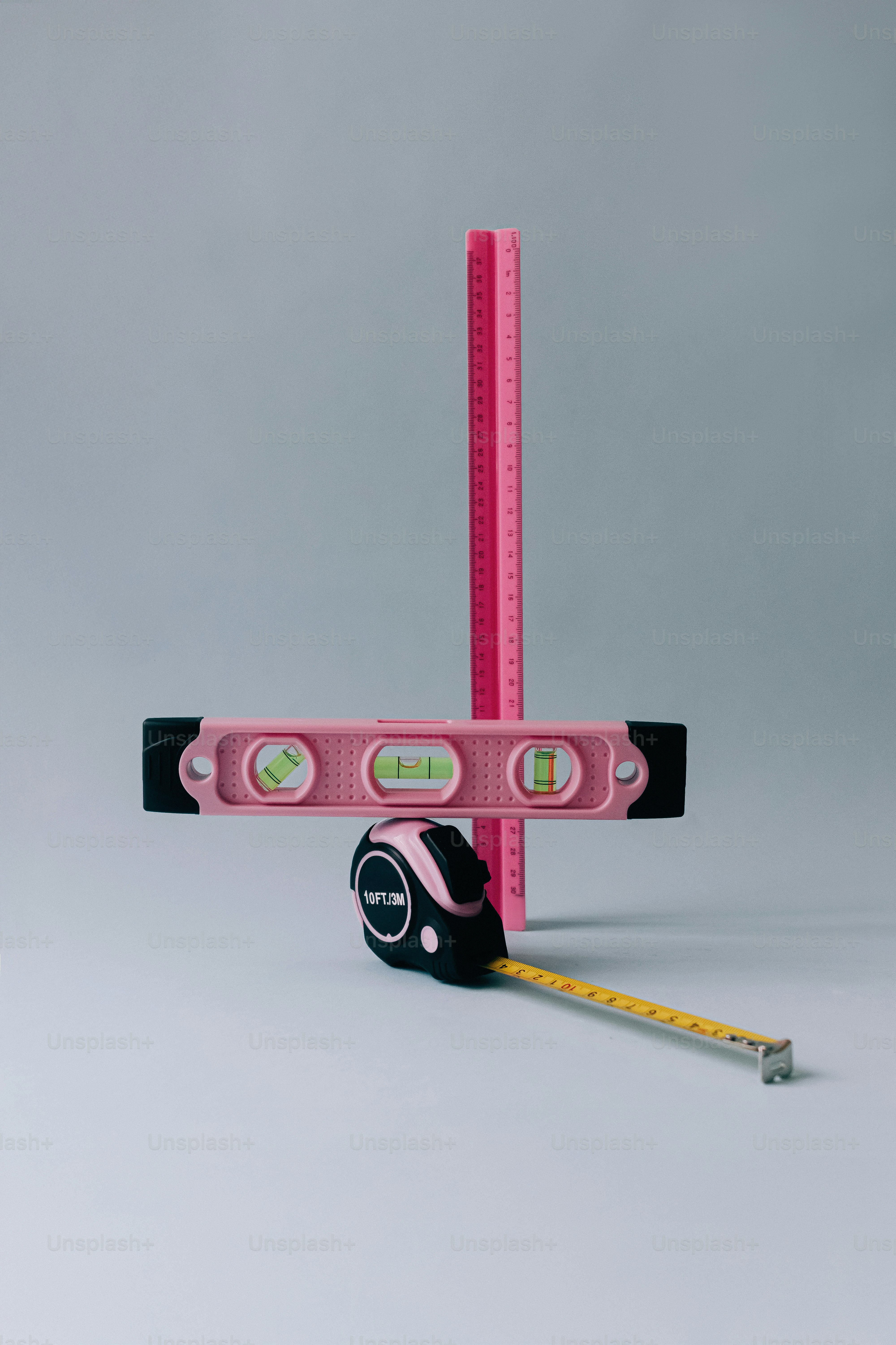 A pink spirit level, a pink ruler, and a black tape measure.