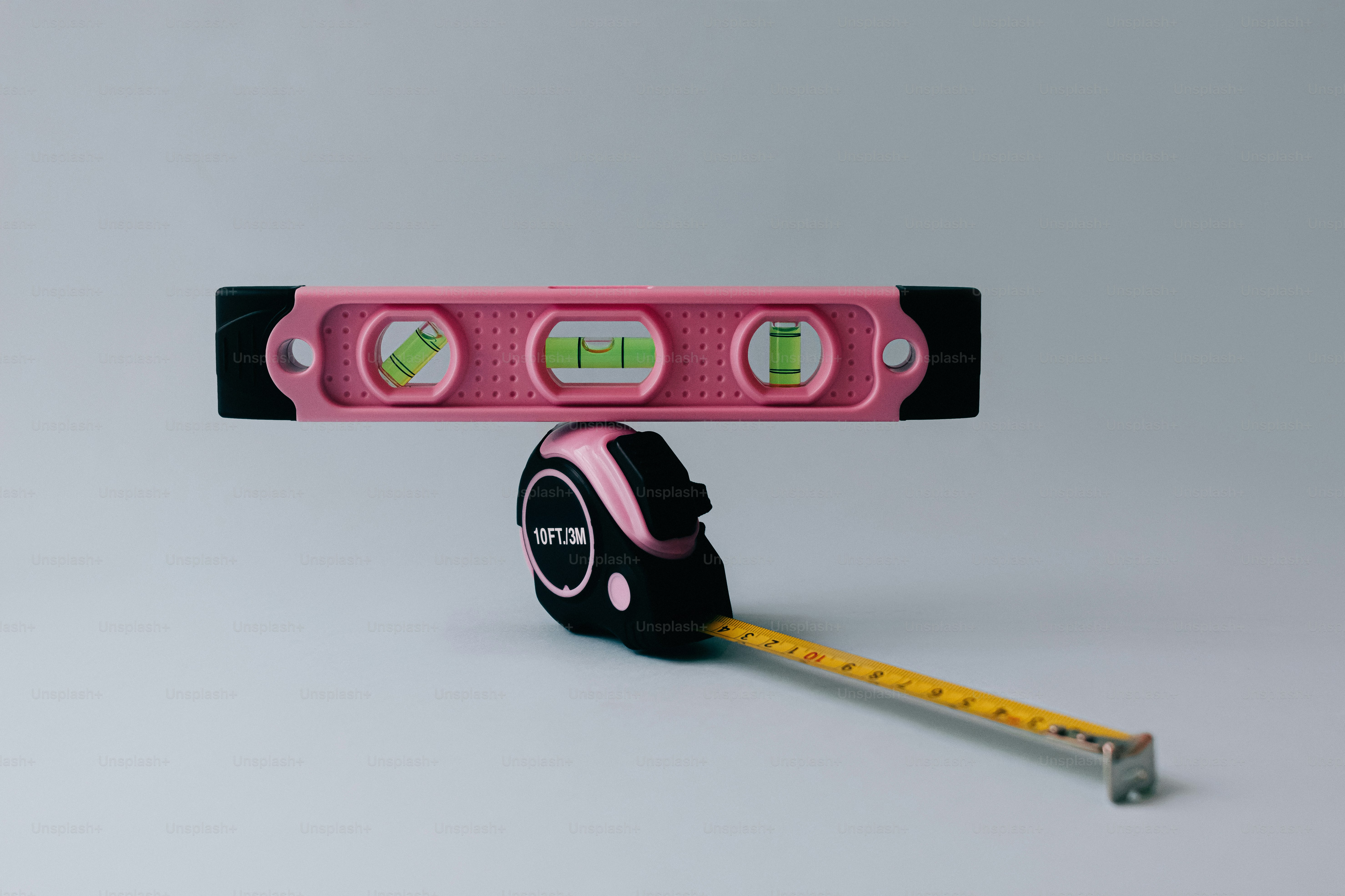 A pink spirit level balanced on a pink and black tape measure.