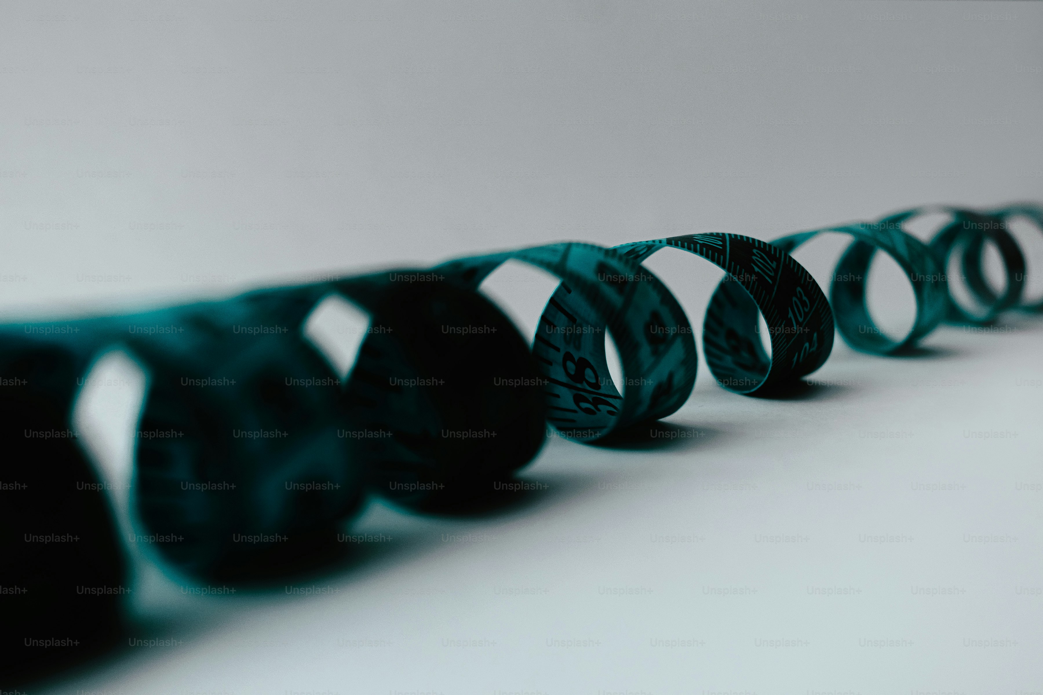 A teal measuring tape coiled in a line on a light grey surface.