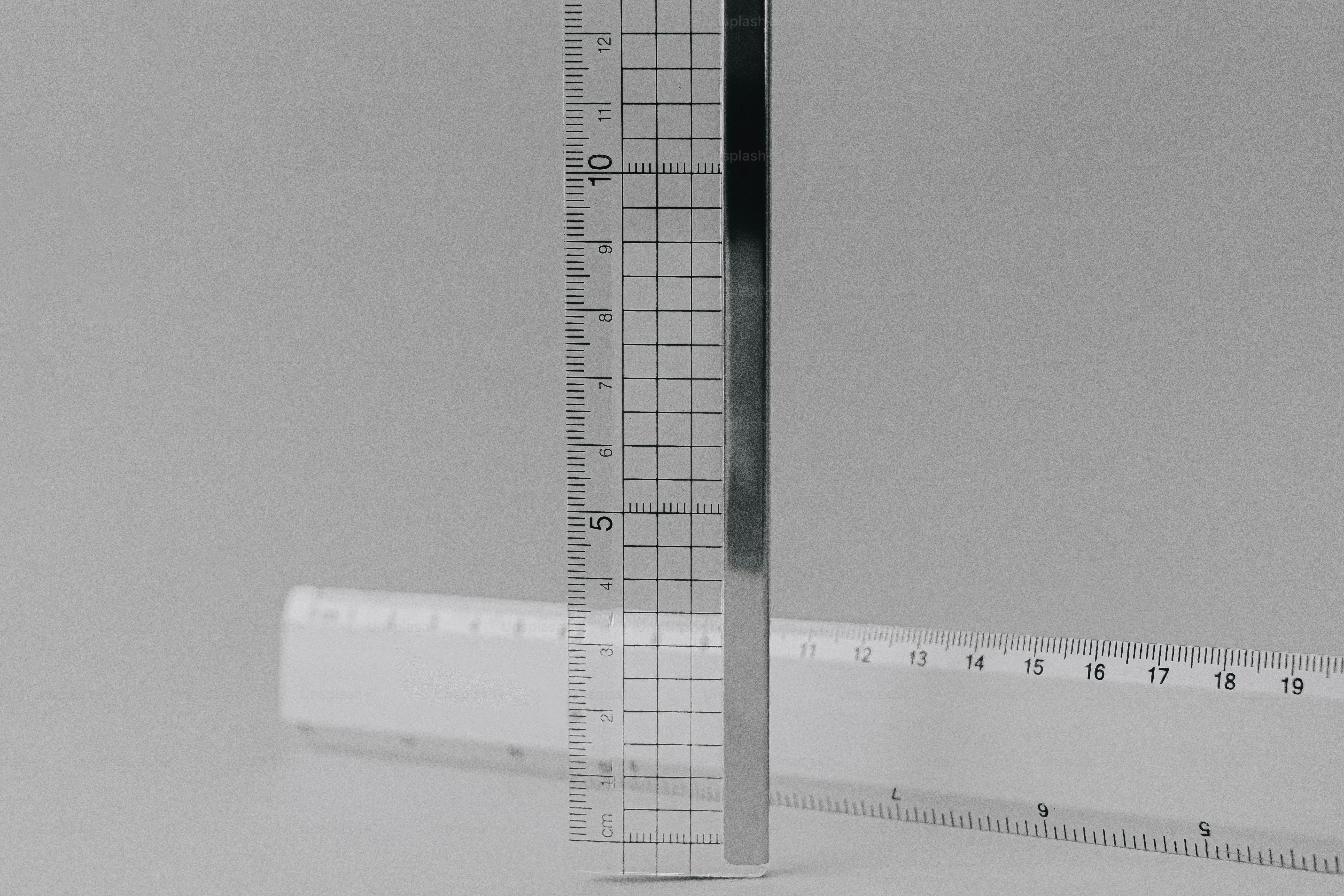 A vertical clear plastic ruler with a grid pattern against a horizontal white ruler.