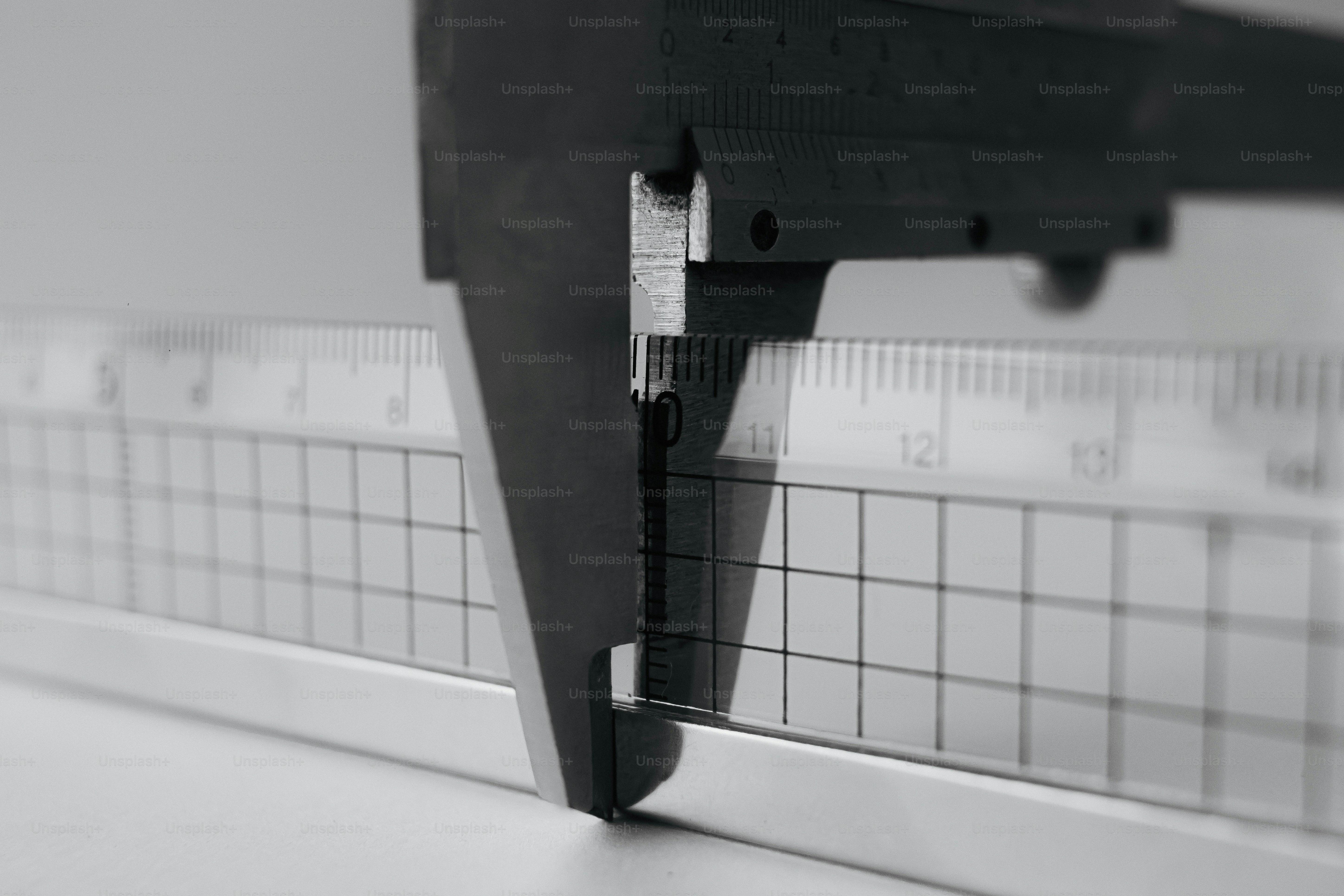 A metal caliper measuring the thickness of a grid-patterned ruler.