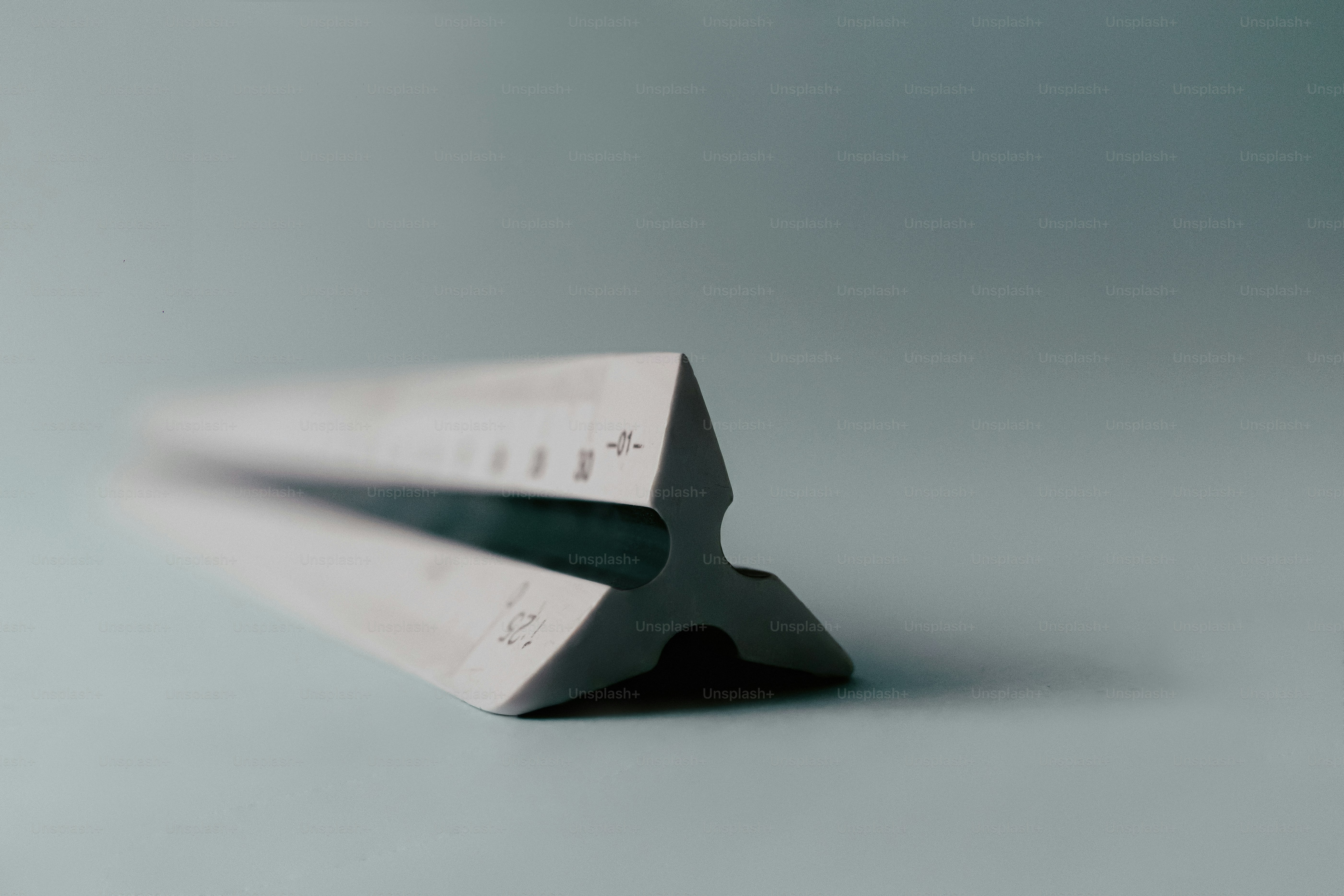 A white triangular architectural scale ruler on a plain grey surface.