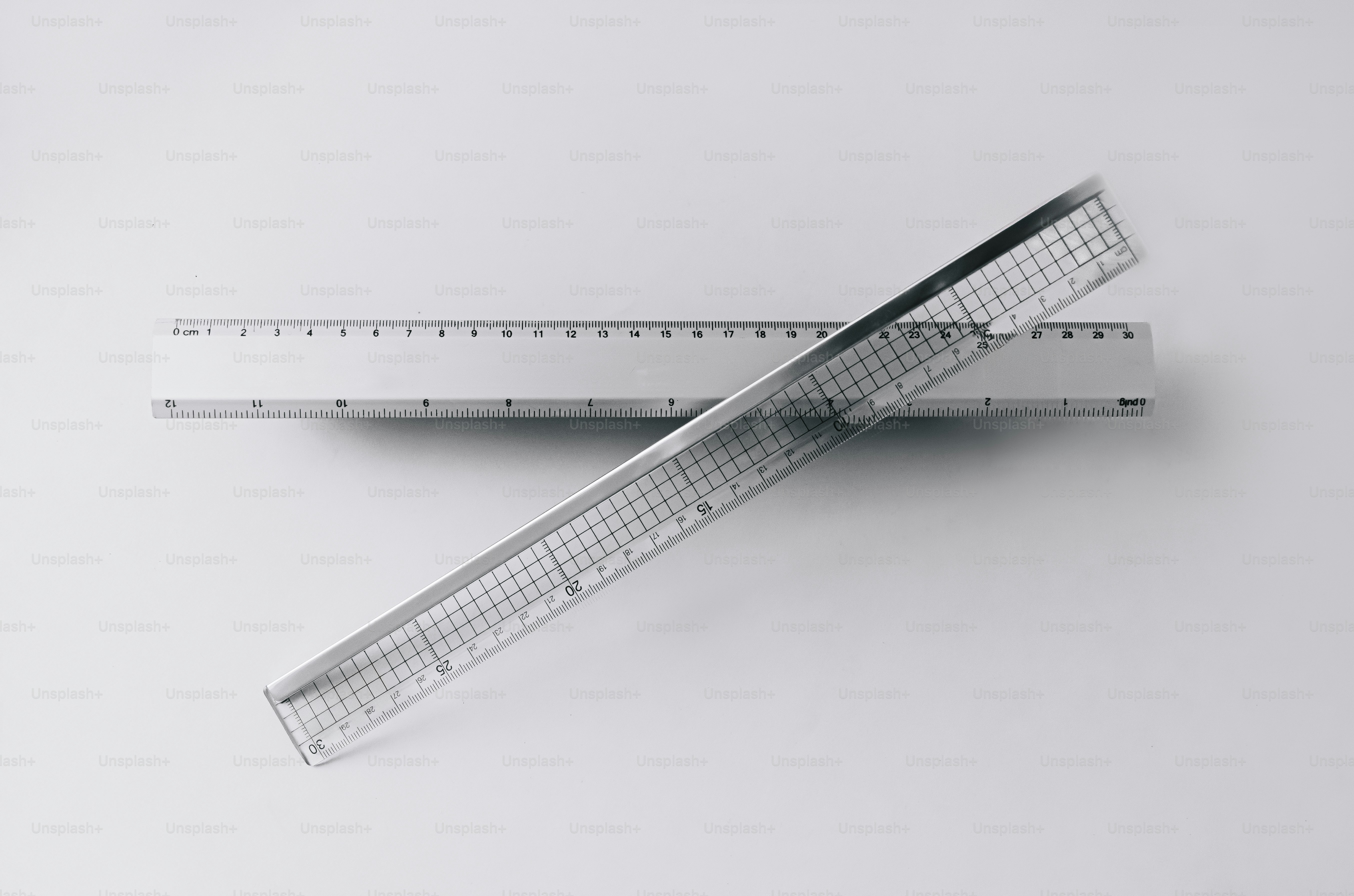 Two clear plastic rulers crossed over each other on a light grey surface.
