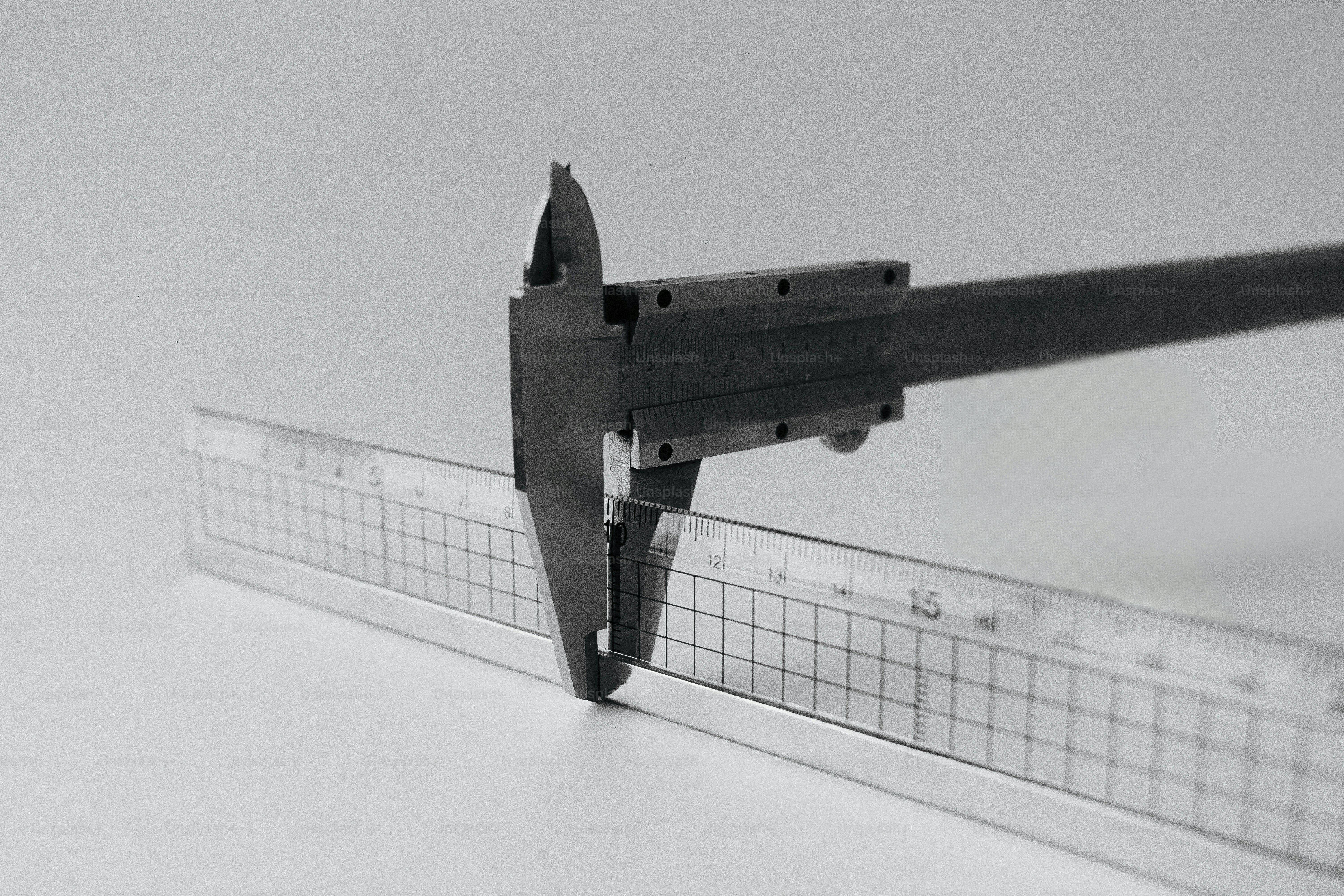 A metal caliper measuring the thickness of a clear plastic ruler.