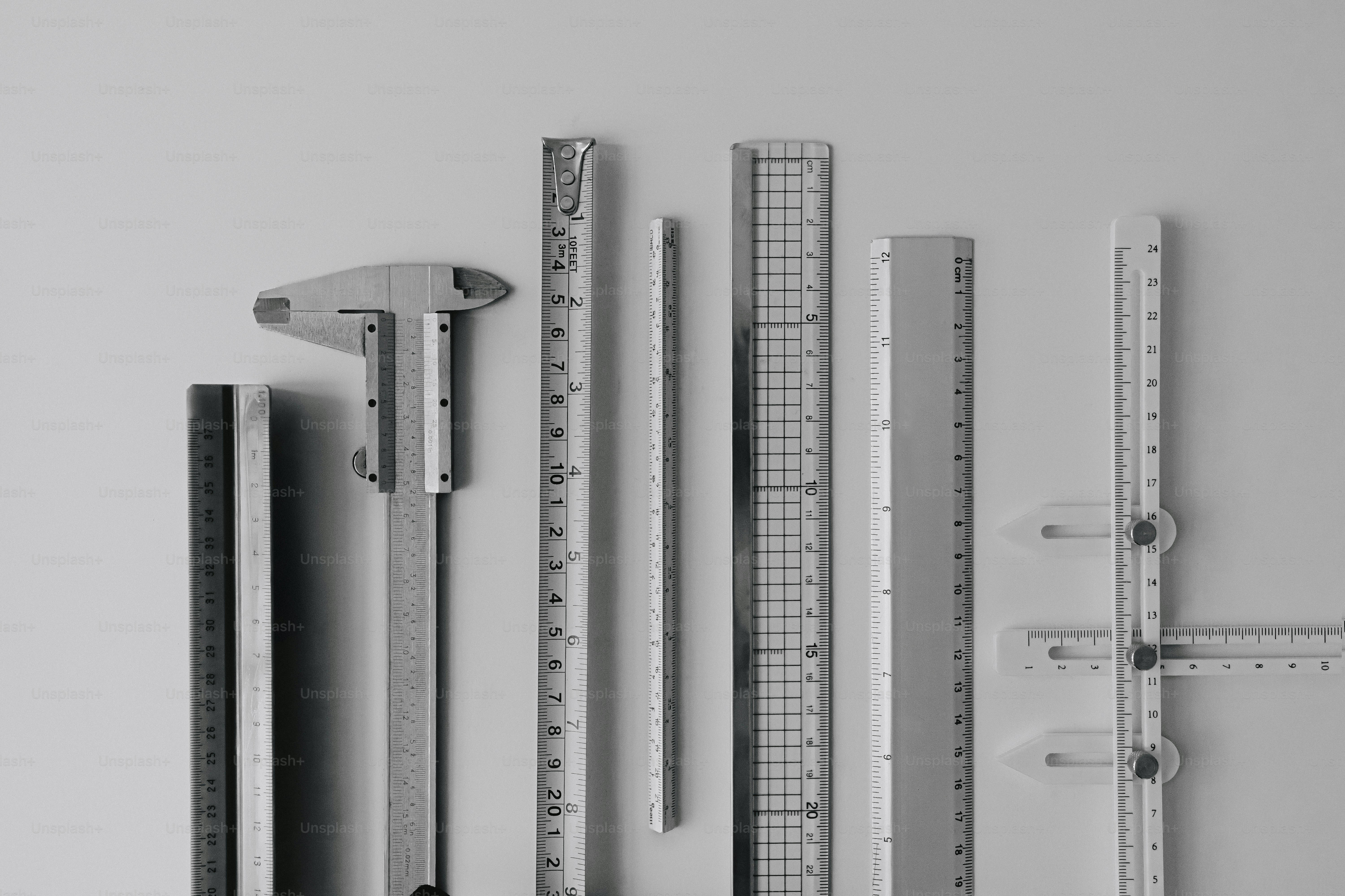 A collection of various metal measuring tools and rulers arranged on a white surface.
