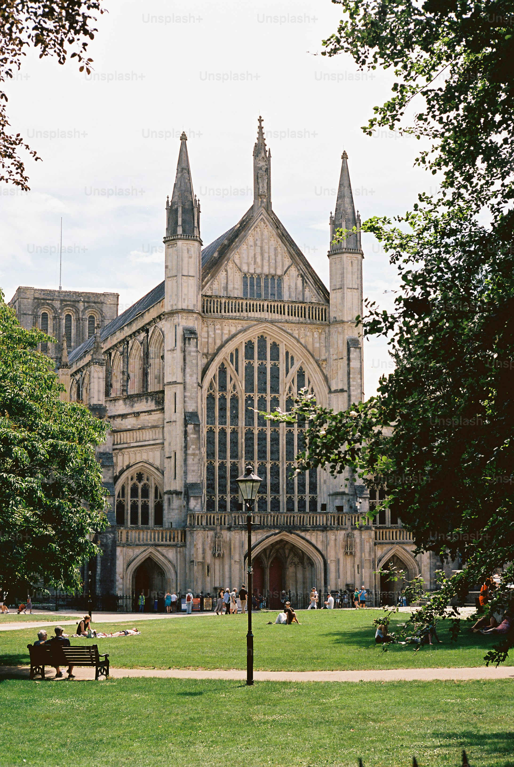 People relaxing on a green lawn before the stone facade of Winchester Cathedral