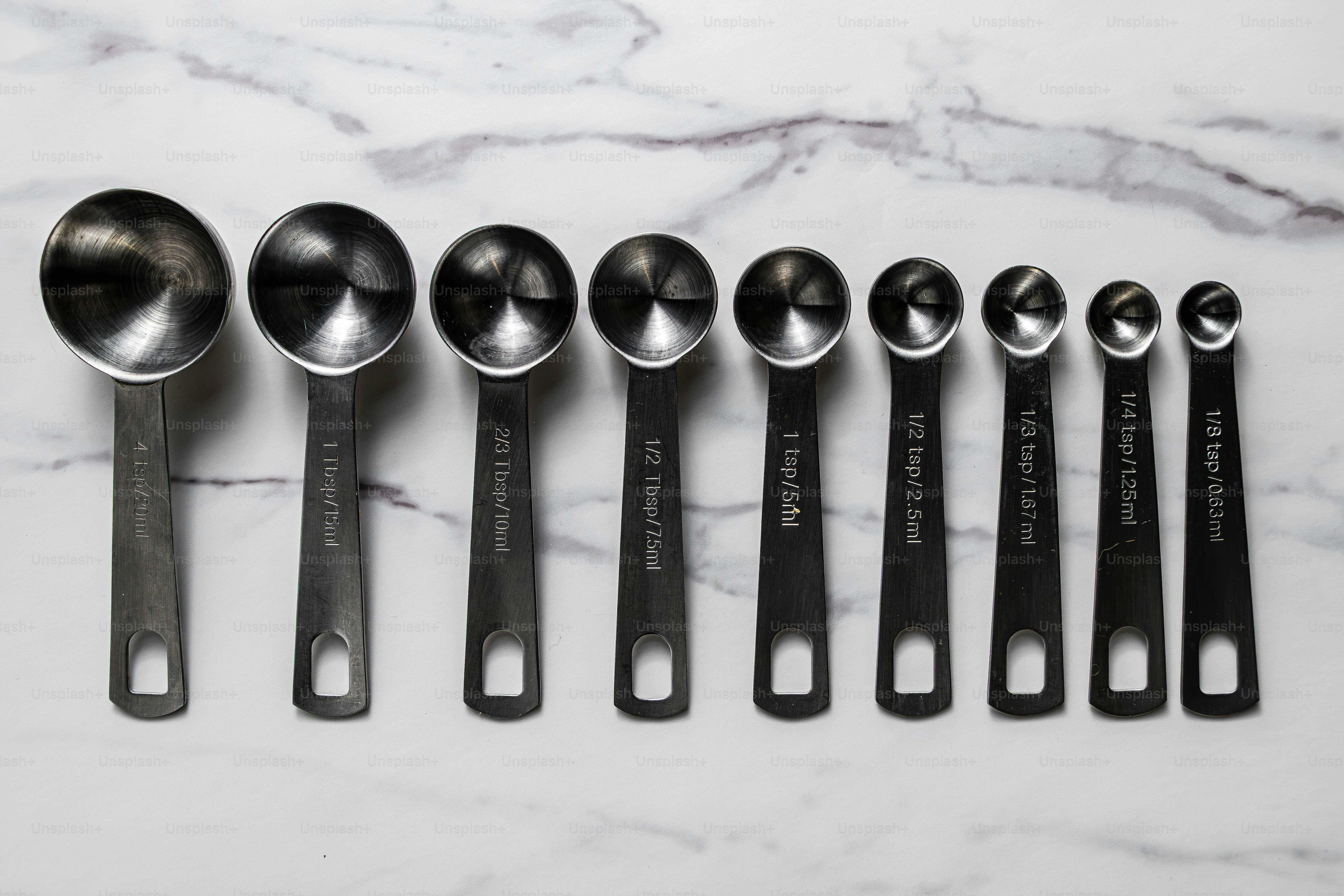 Nine stainless steel measuring spoons lined up on a white marble surface