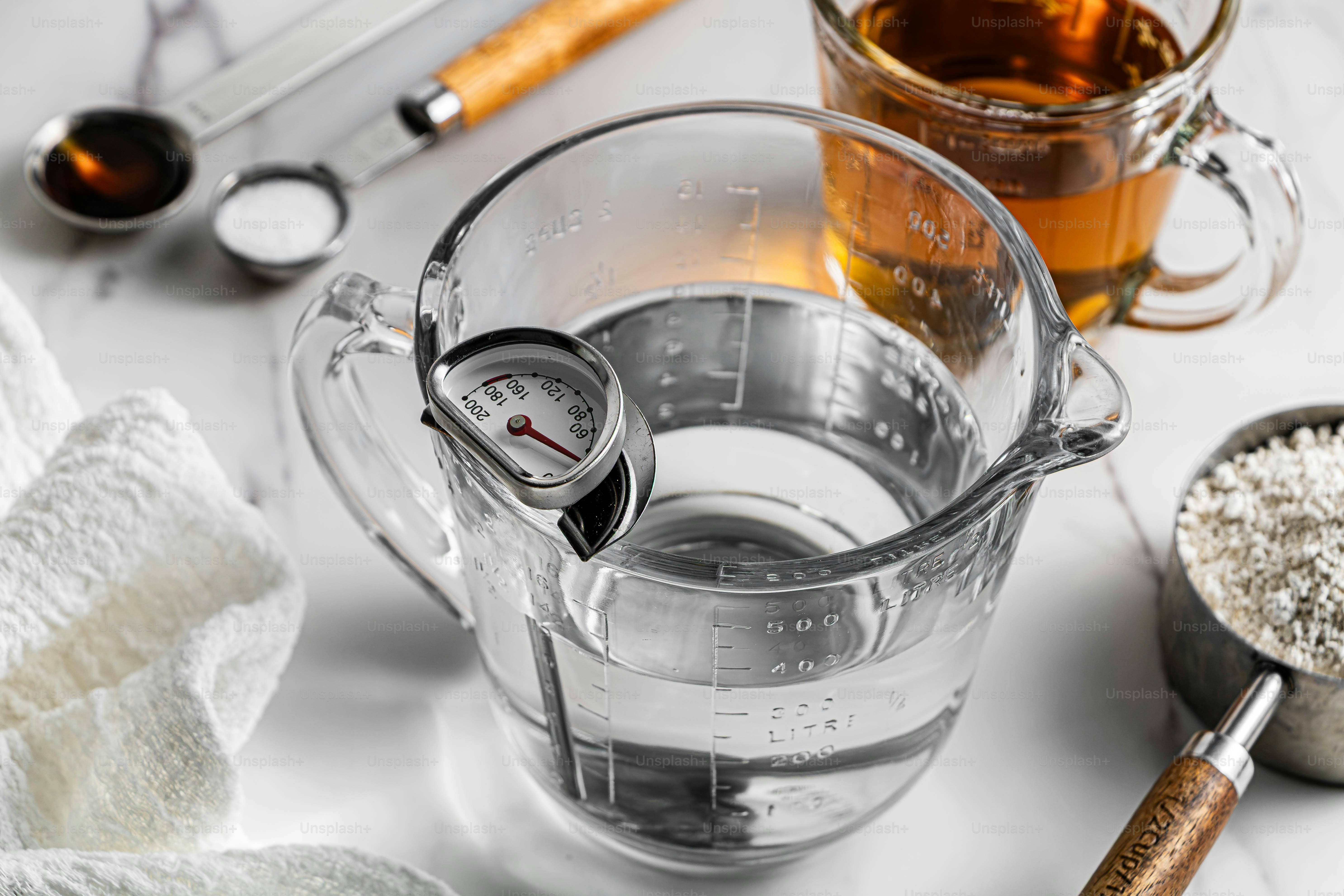 A glass measuring cup with water and a thermometer on a marble surface
