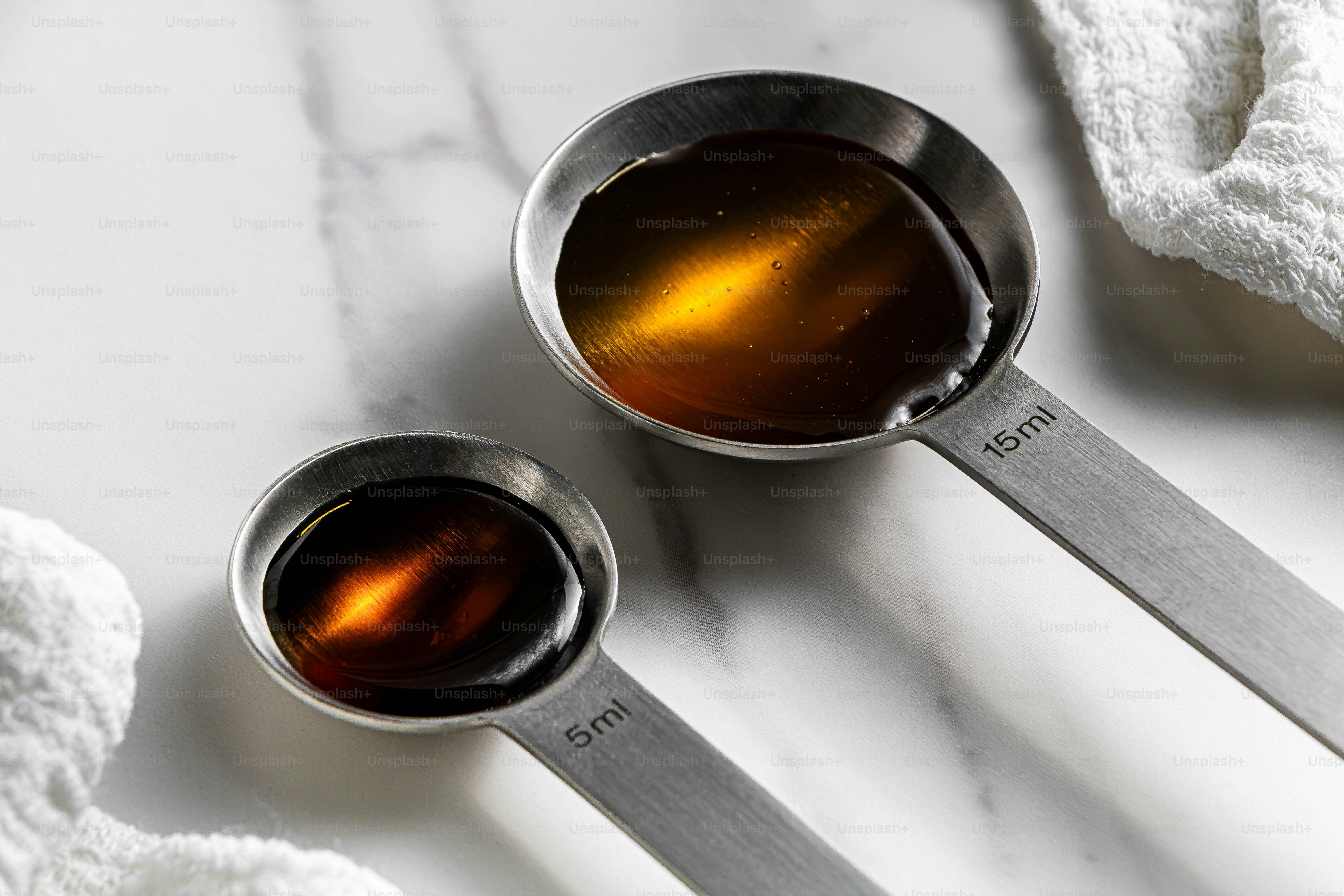 Two stainless steel measuring spoons filled with dark syrup on a marble surface