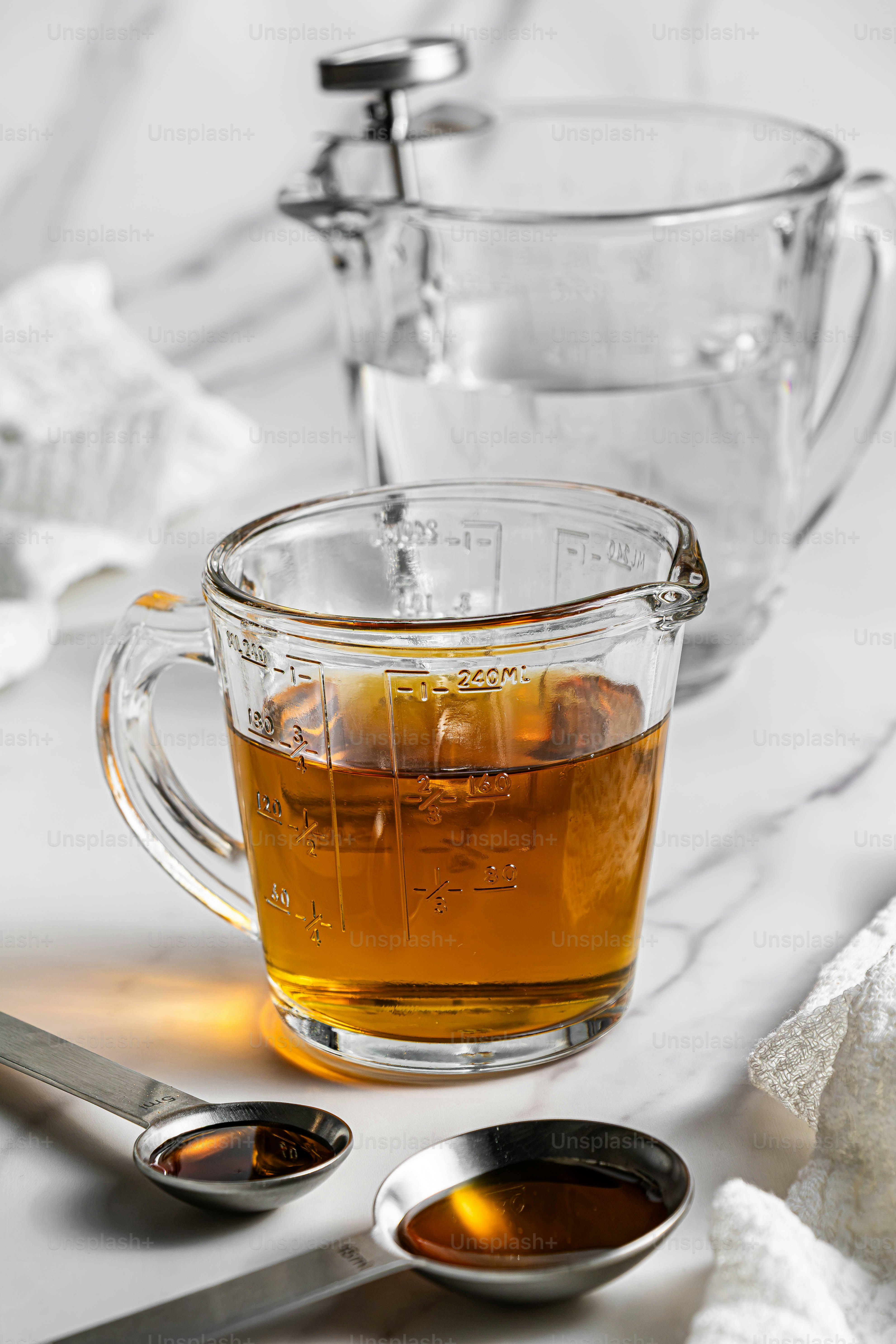 Amber liquid in a glass measuring cup with two metal spoons on marble