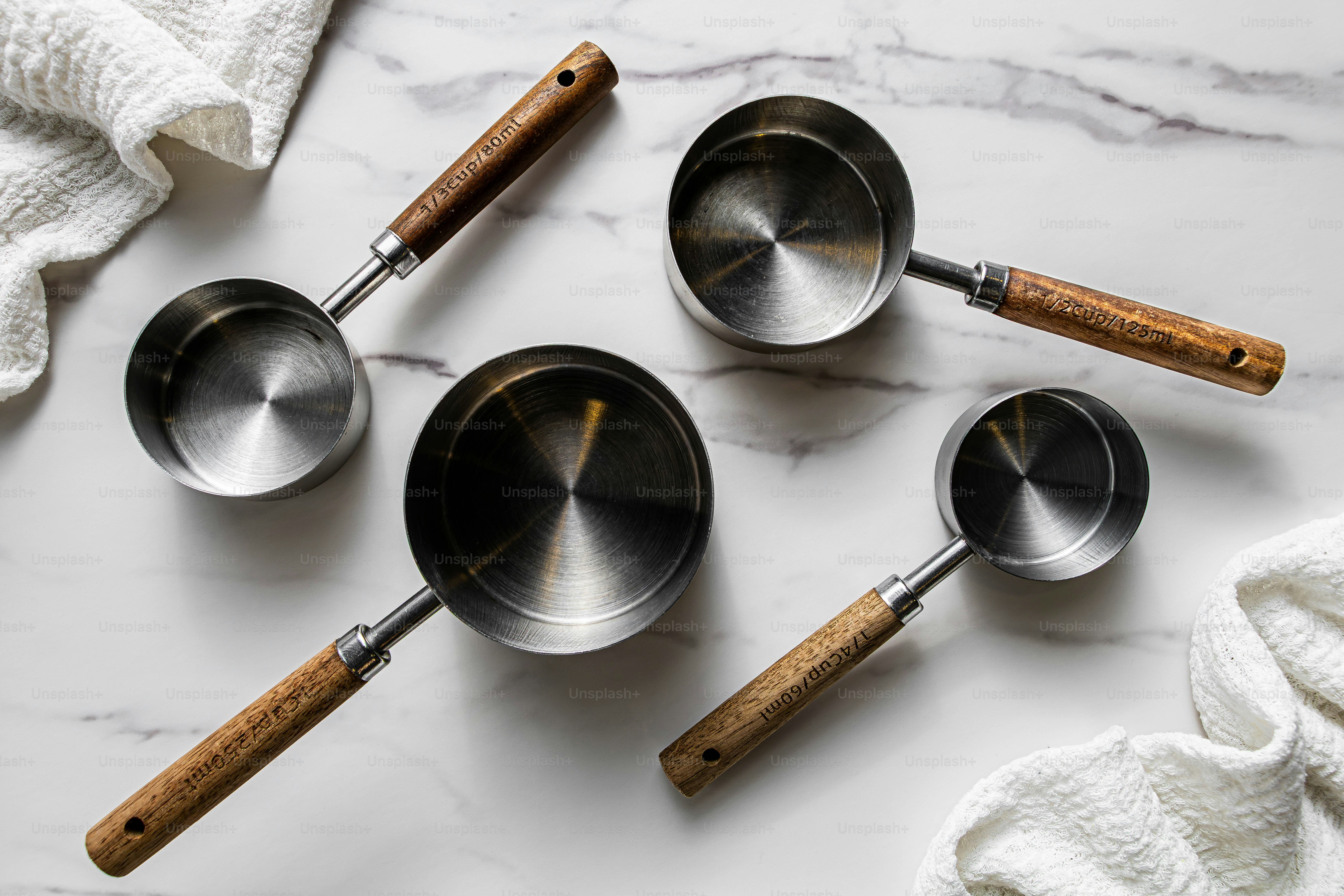 Cuatro tazas métricas de acero inoxidable con asas de madera sobre una superficie de mármol blanco