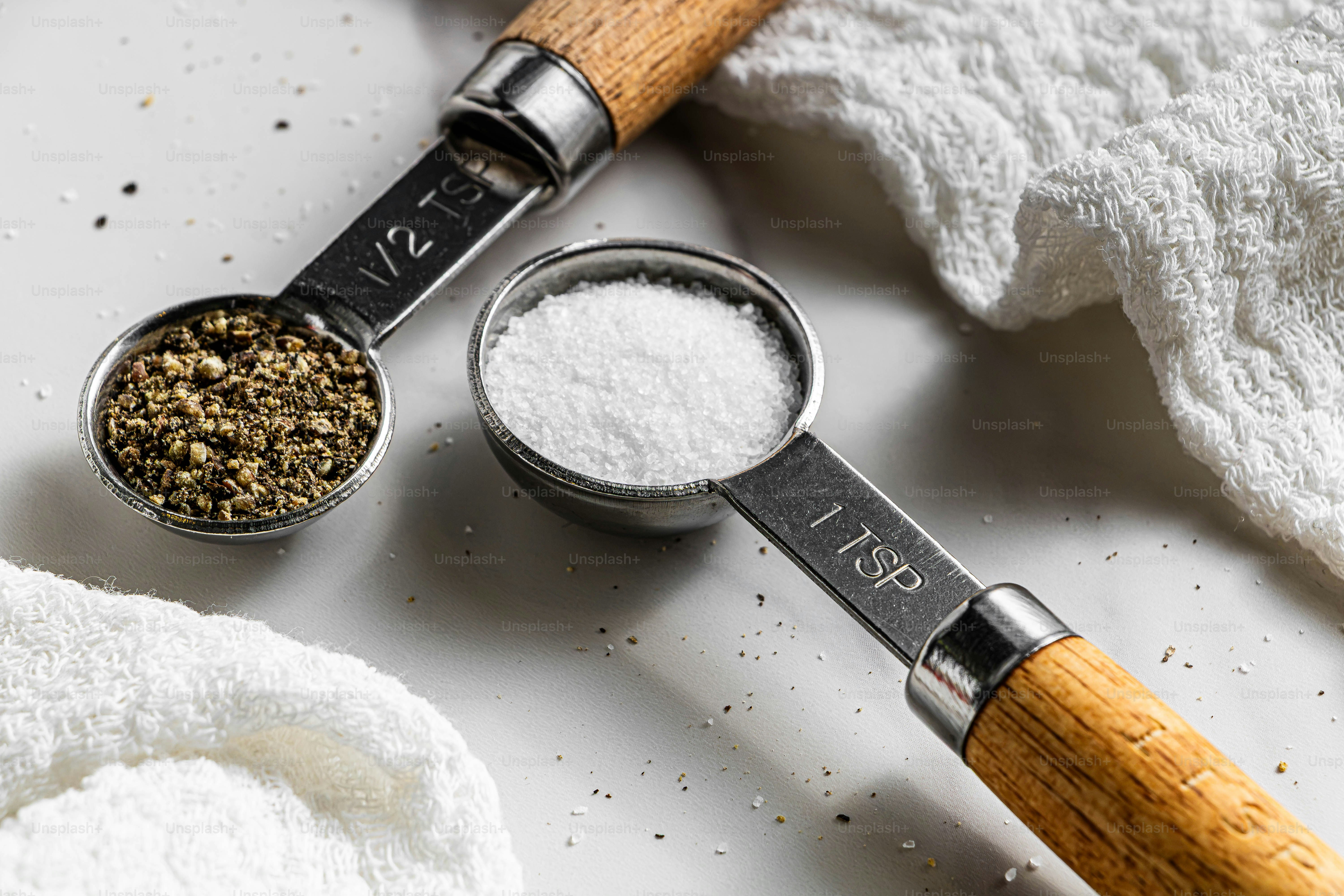 Measuring spoons with ground black pepper and salt on a white surface