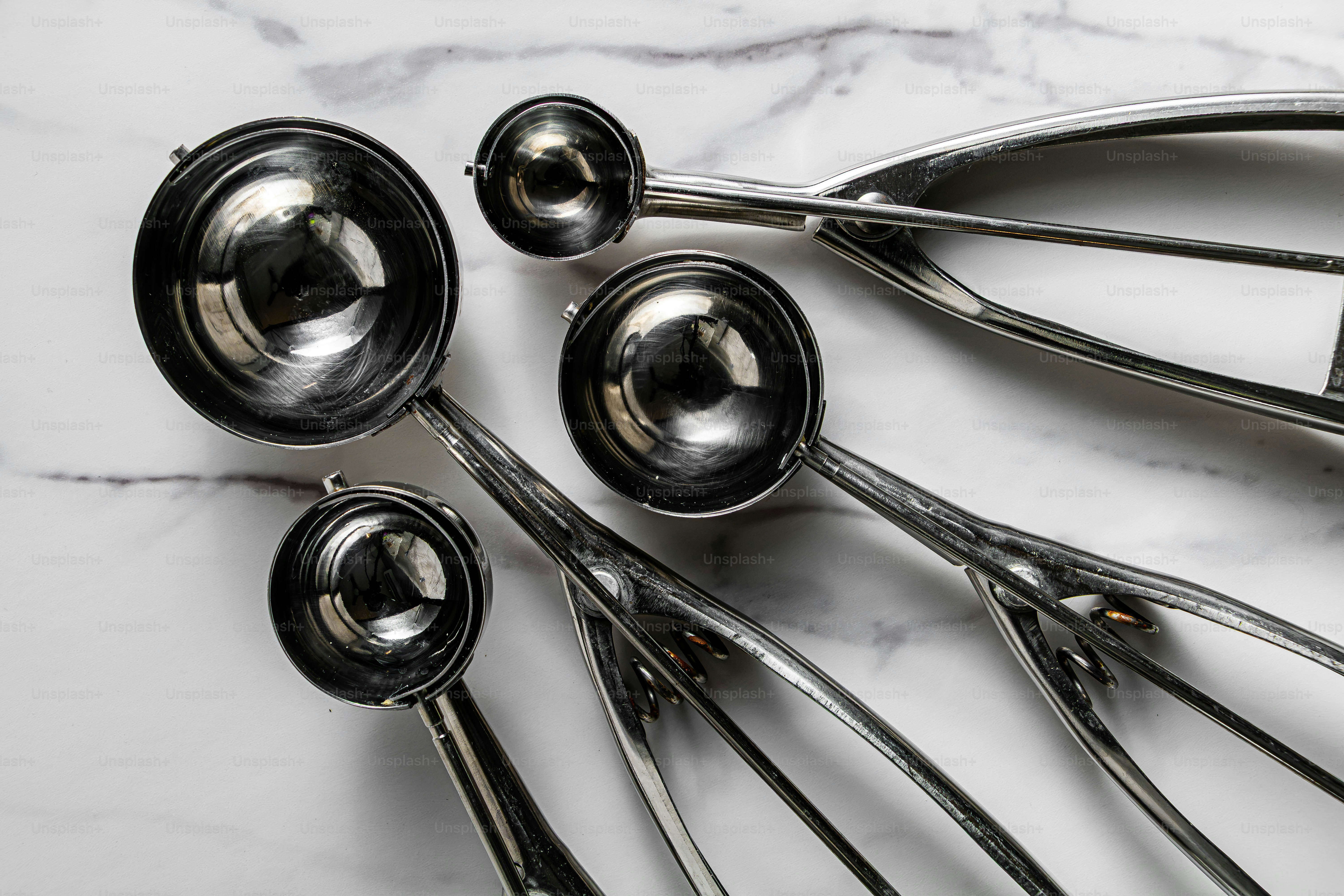 Four stainless steel cookie scoops of varying sizes on a white marble surface