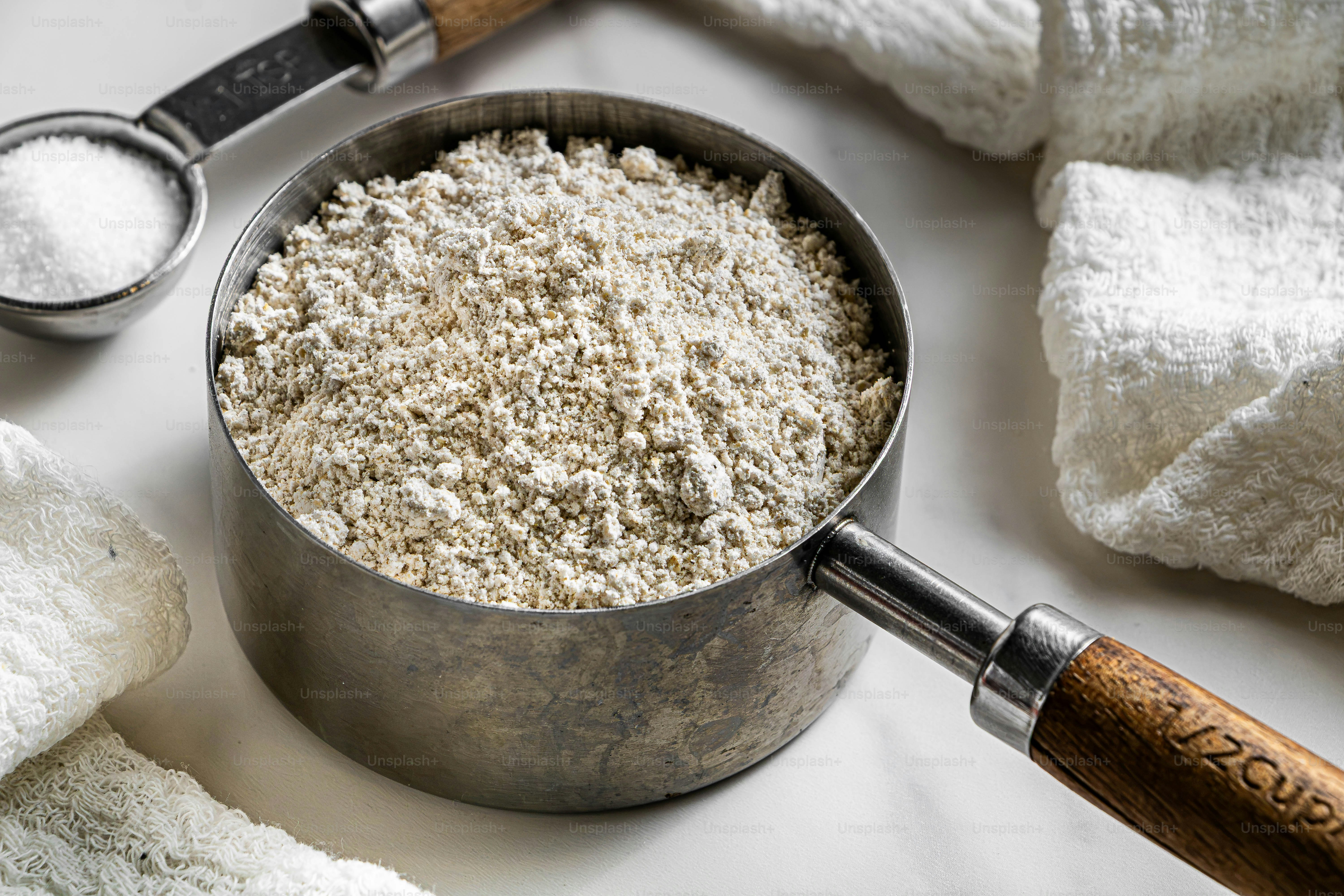 A metal measuring cup filled with flour beside a small spoon of salt