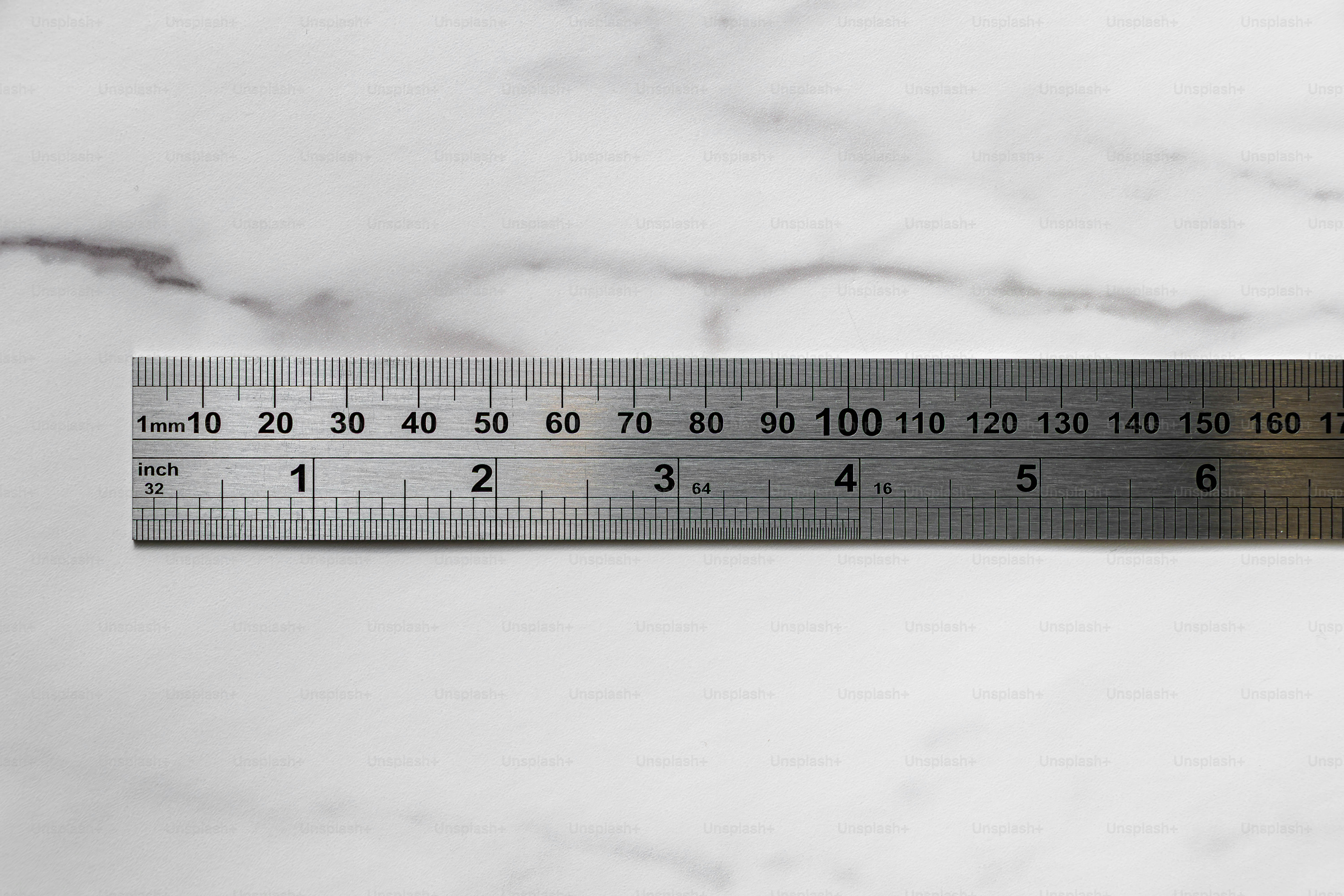 A stainless steel ruler with metric and imperial markings on a white marble surface