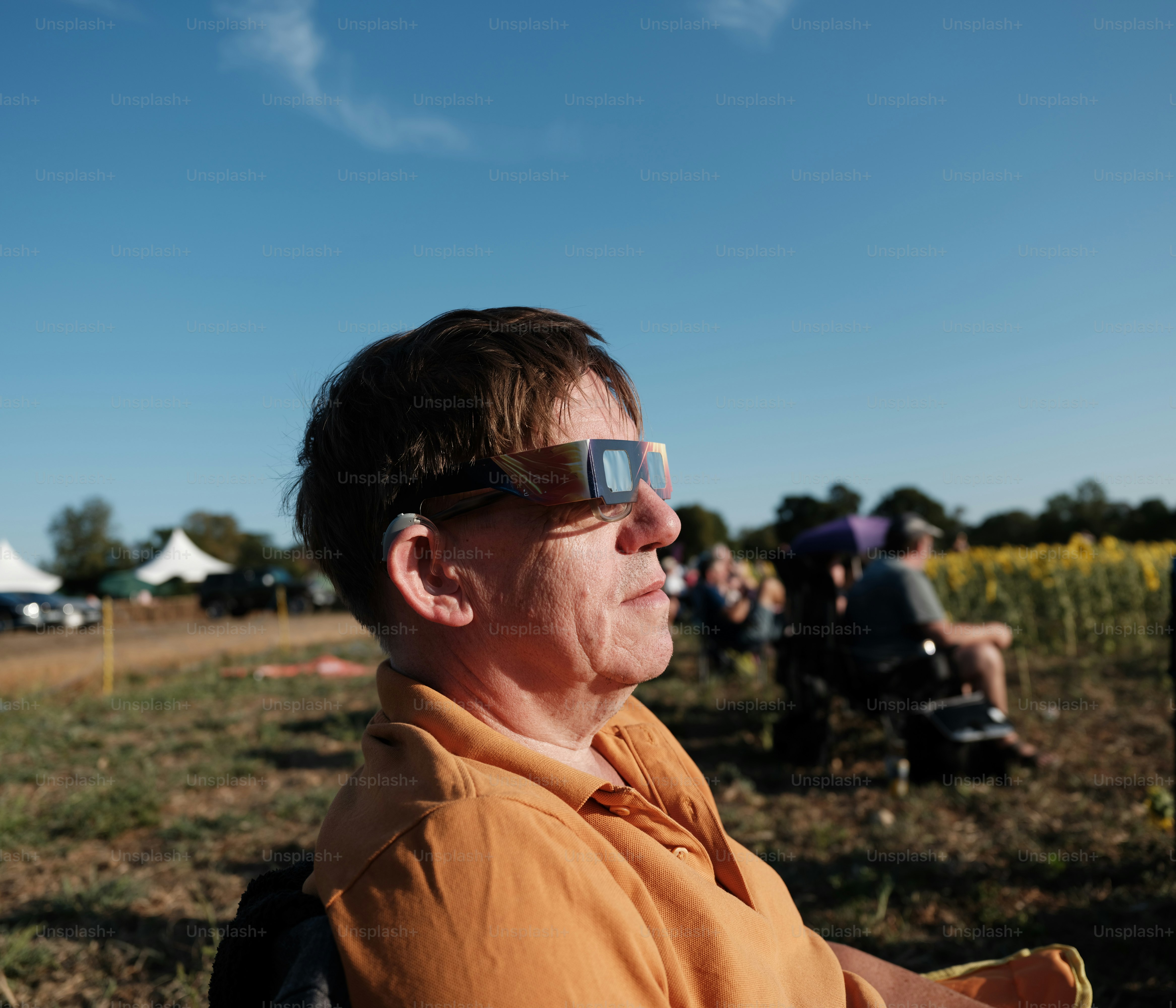 A man wearing solar eclipse glasses in a field with other people nearby.