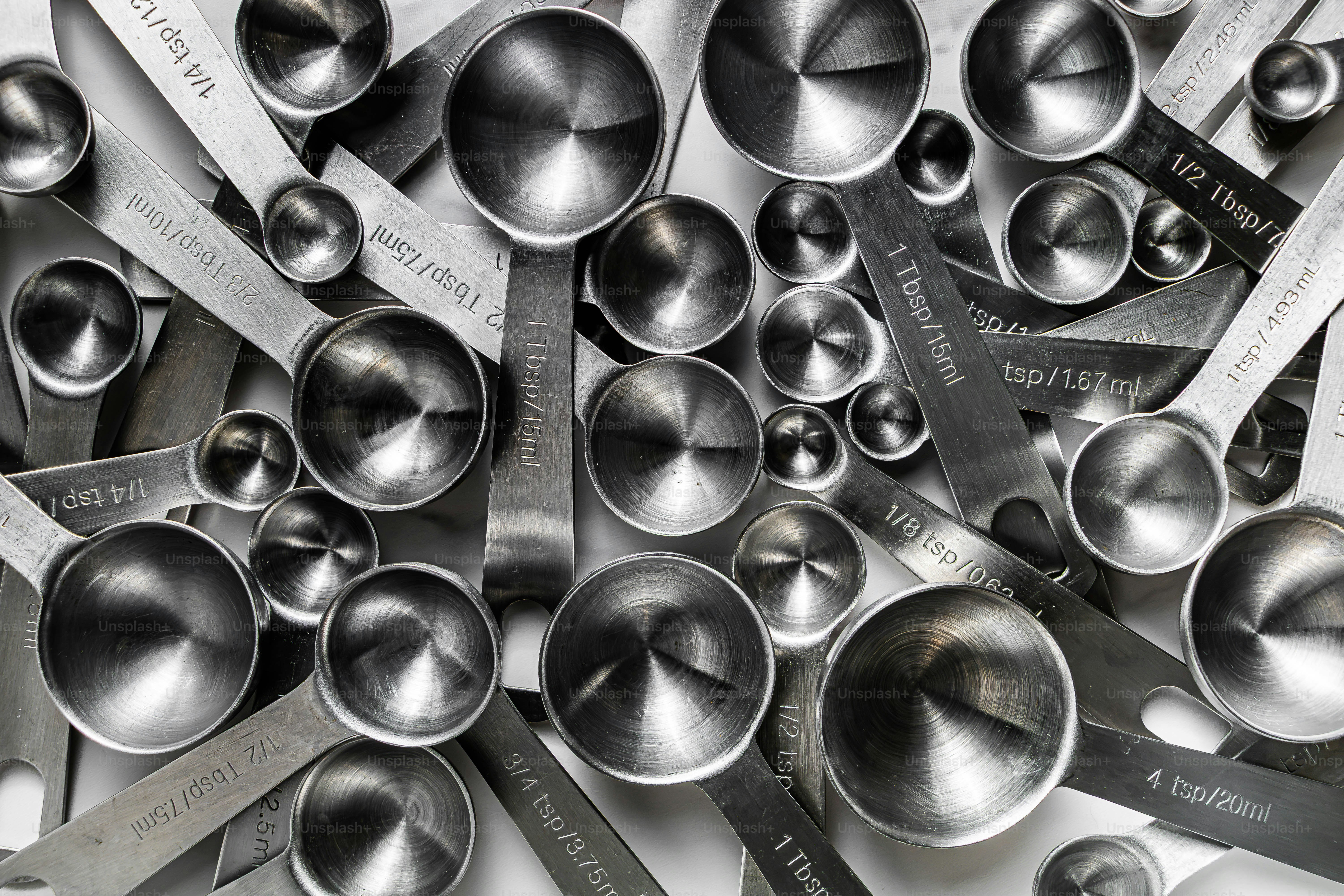 Una collezione di cucchiai di misura in acciaio inox sparsi su una superficie bianca