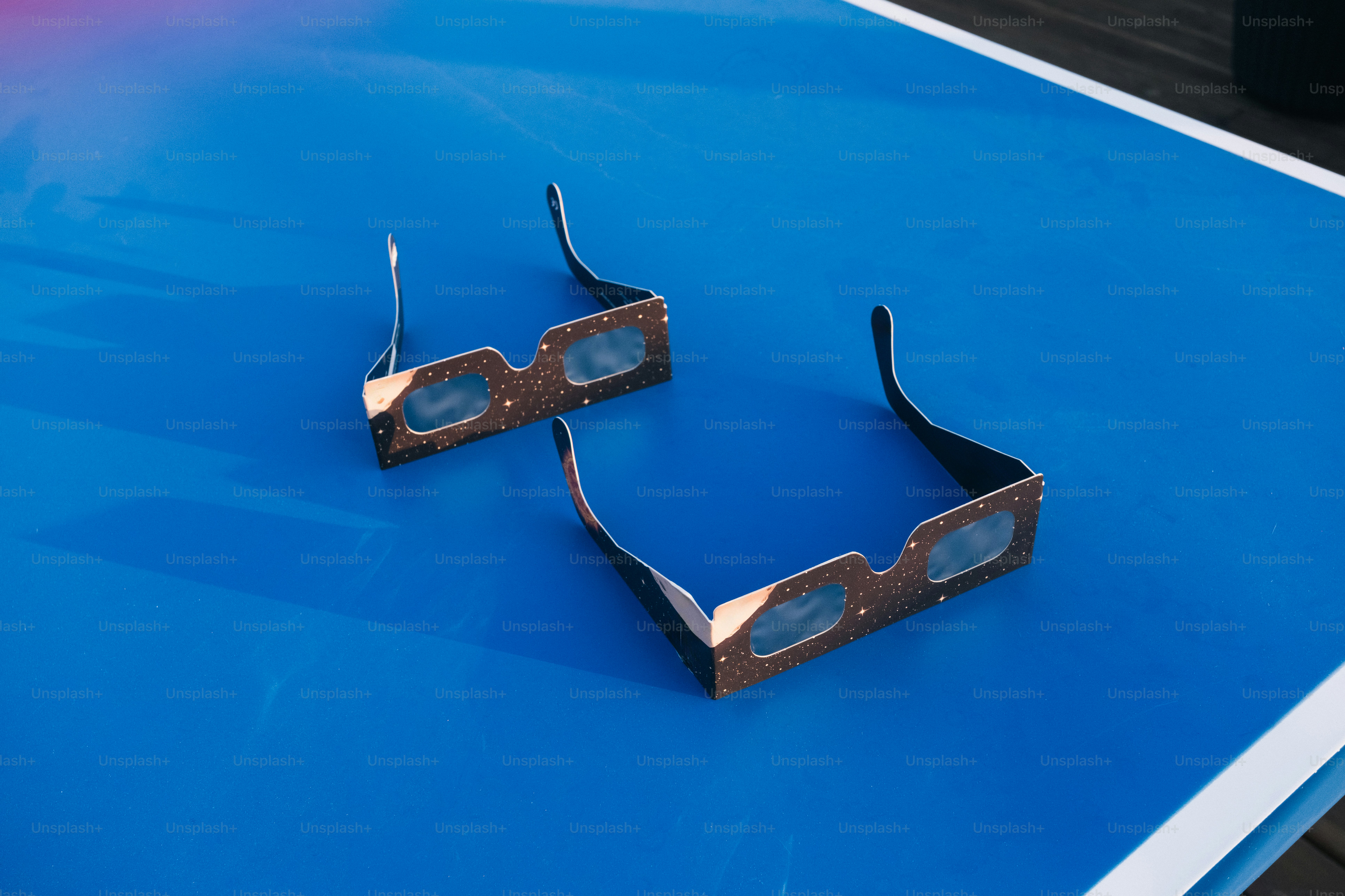 Two pairs of paper eclipse glasses with star patterns on a blue surface.