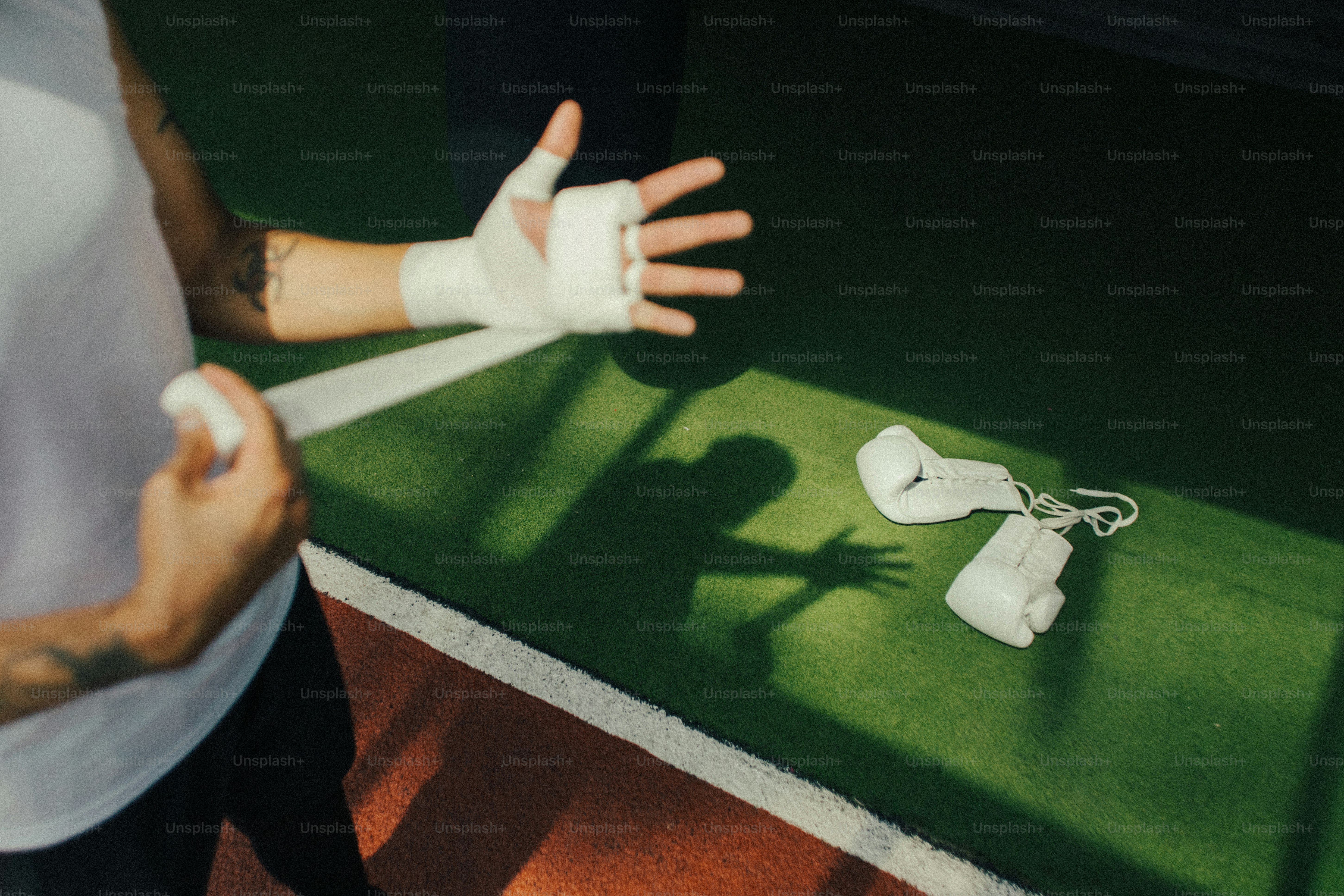 A person wrapping their hands with white tape beside white boxing gloves on turf.