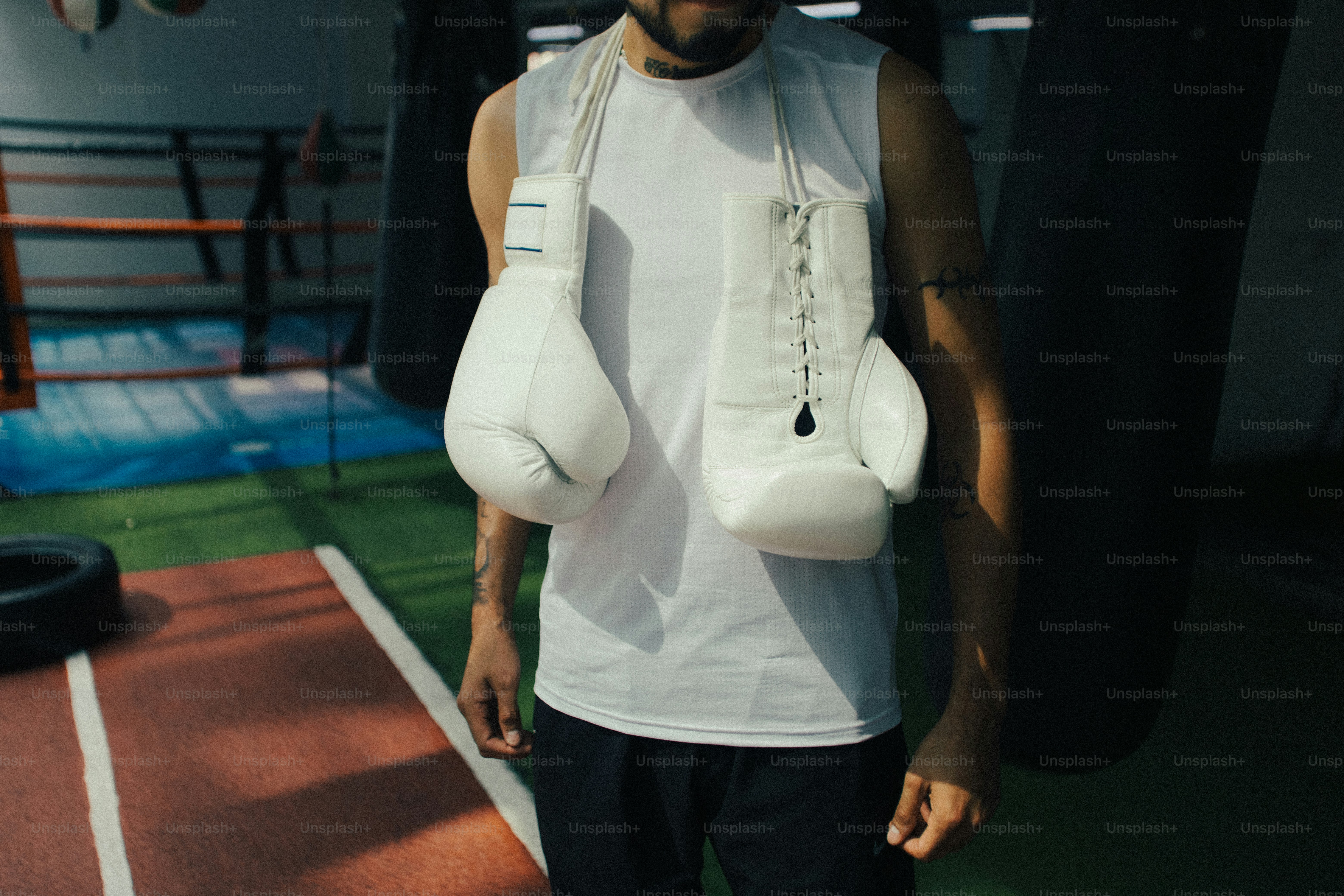 Una persona con una camiseta blanca de tirantes y guantes de boxeo blancos colgados del cuello