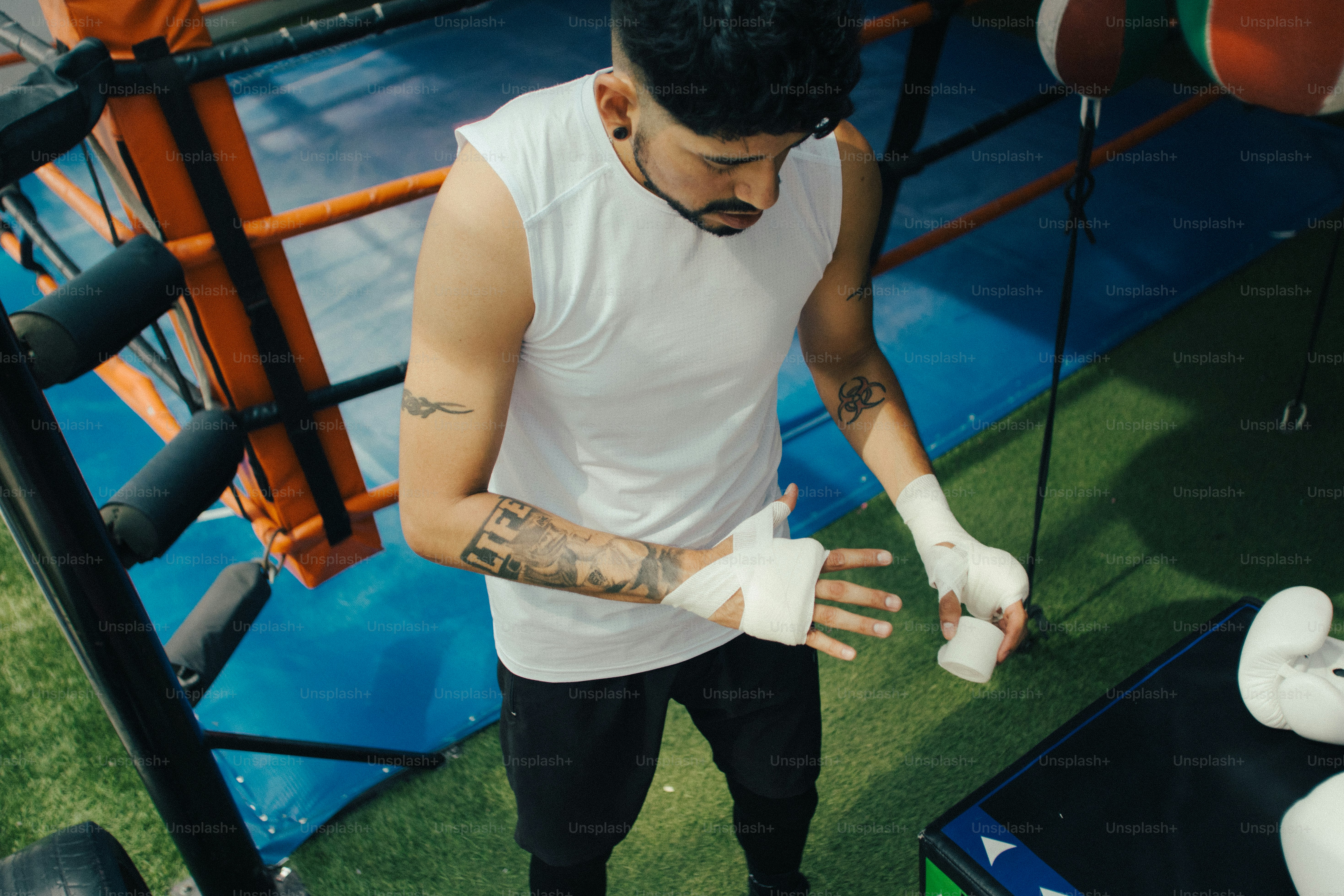 A man in a white tank top wrapping his hands in a boxing gym
