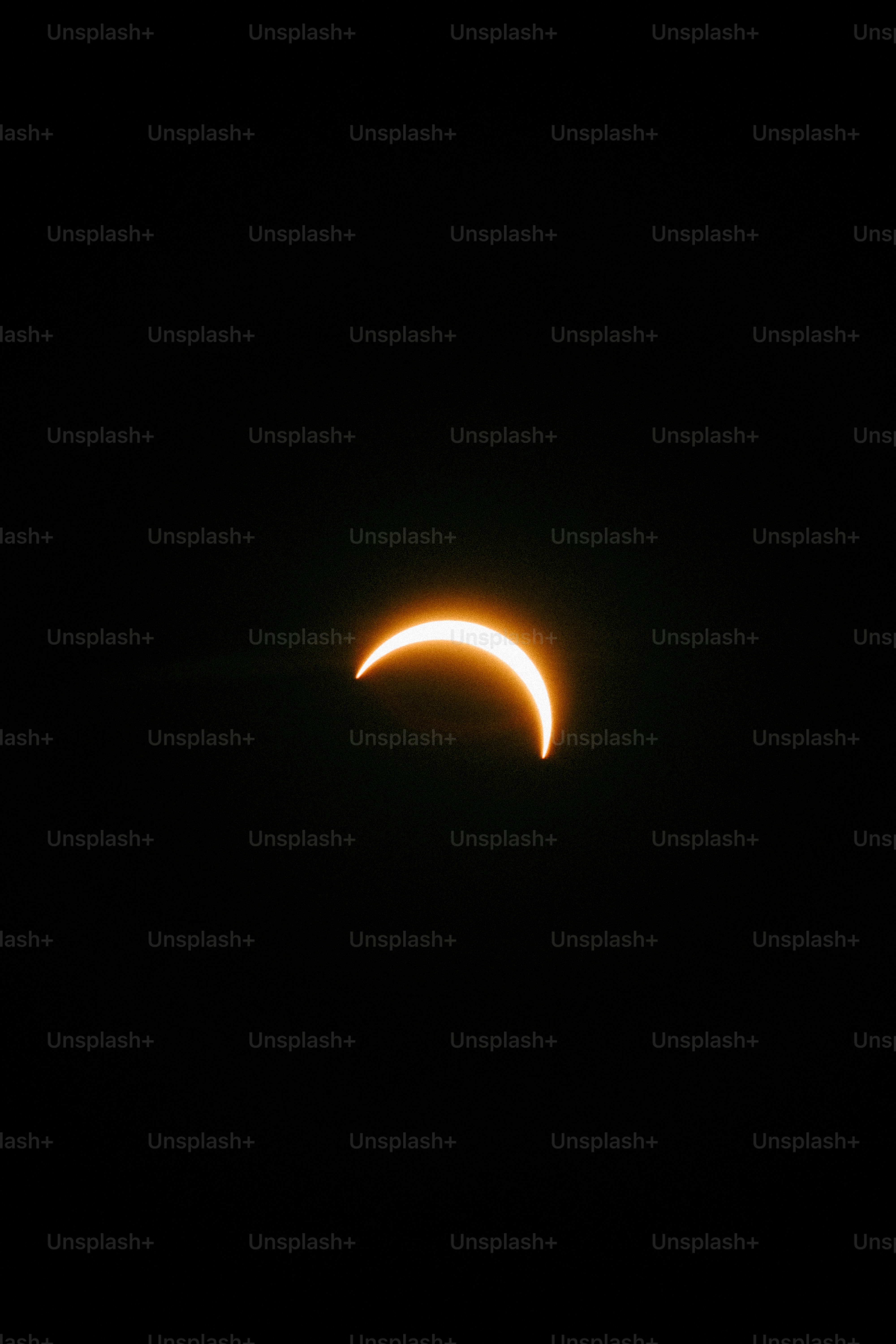 A bright crescent of the sun glowing against a dark black sky.