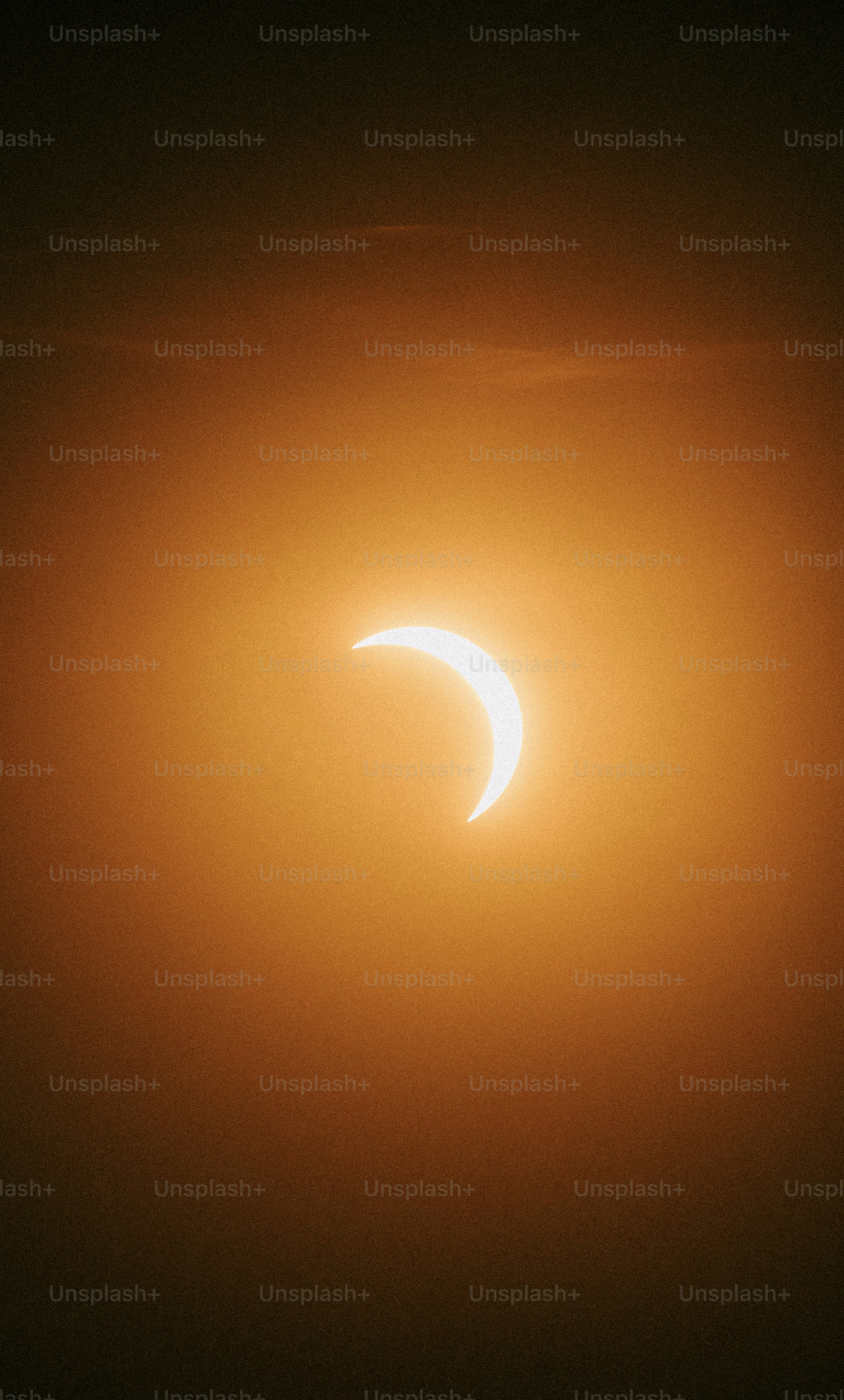 A crescent sun partially eclipsed by the moon in a hazy orange sky.