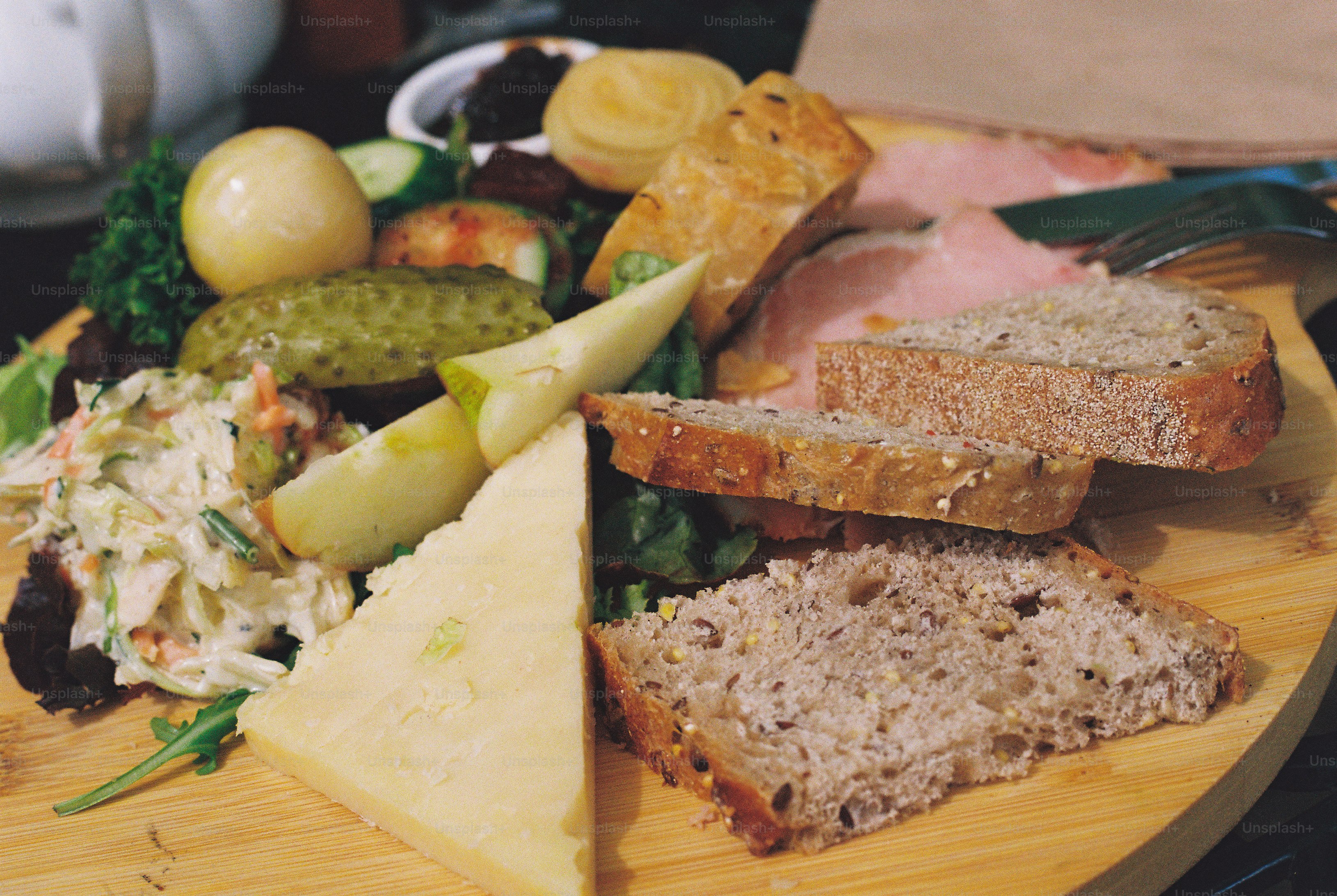A ploughman's lunch with bread, ham, cheese, pickle, and salad on a wooden board.