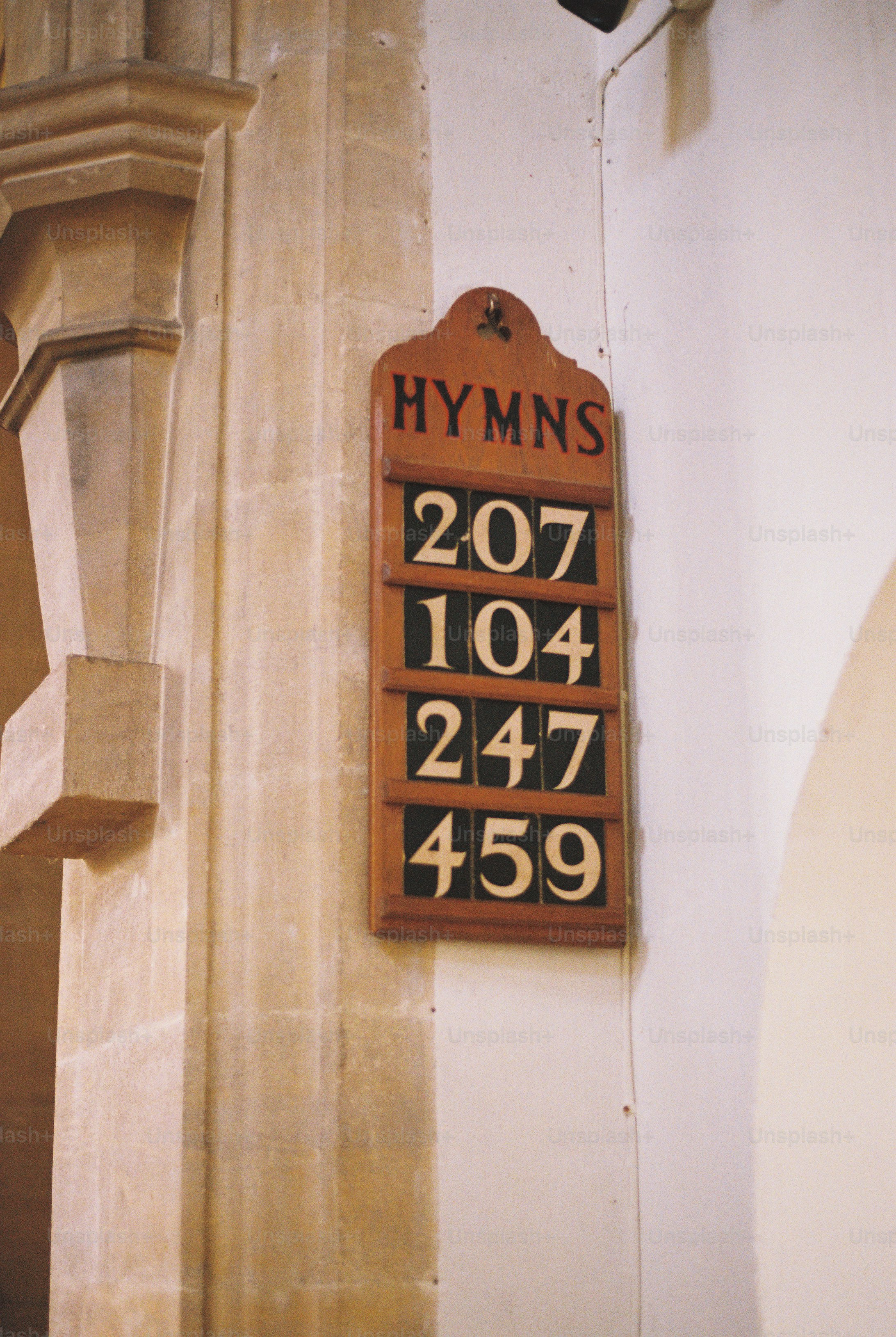 A wooden hymn board with four rows of numbers on a stone church wall.