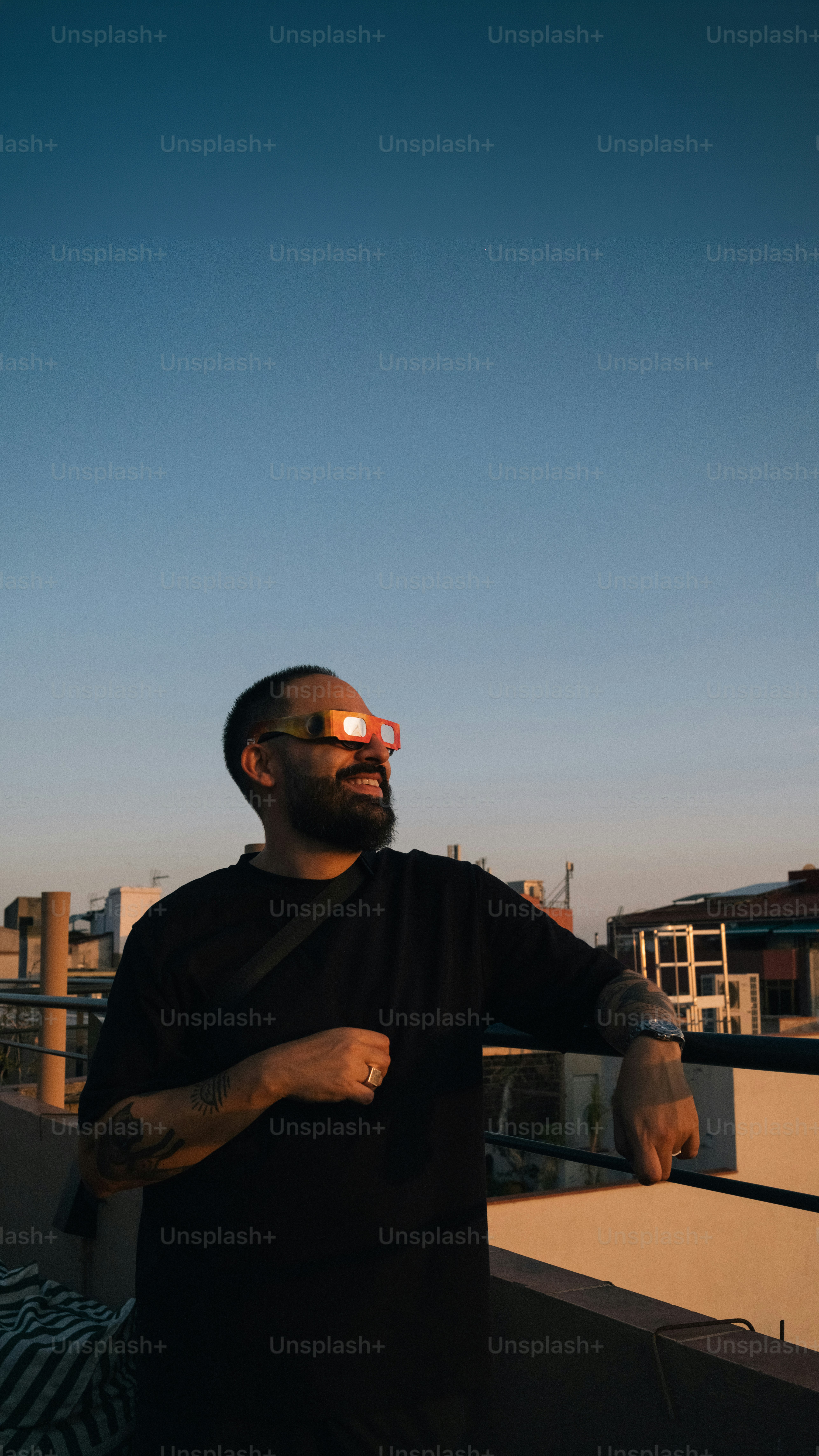A man with a beard wearing eclipse glasses on a rooftop at golden hour