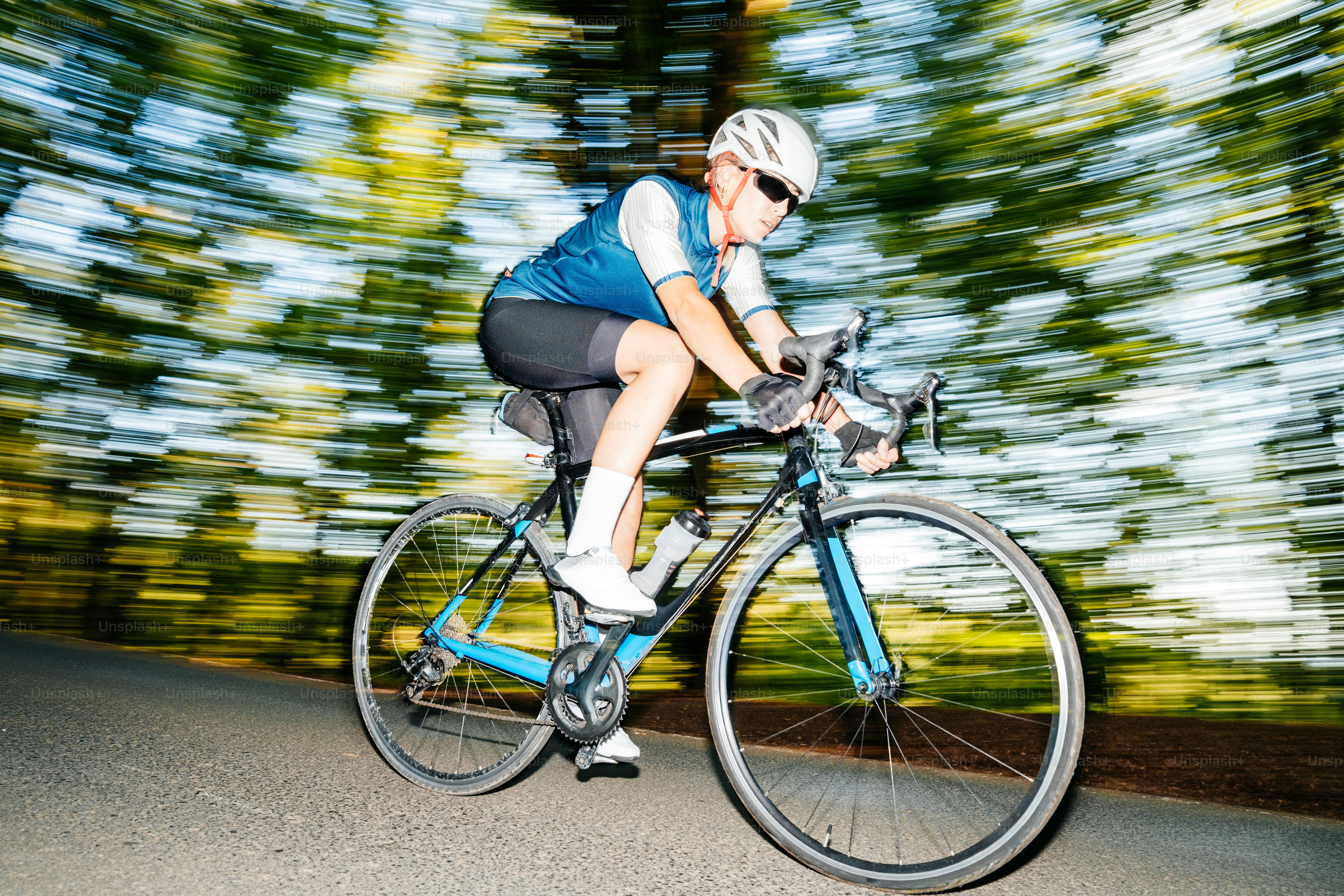 A cyclist in a helmet and blue jersey riding a road bike past trees